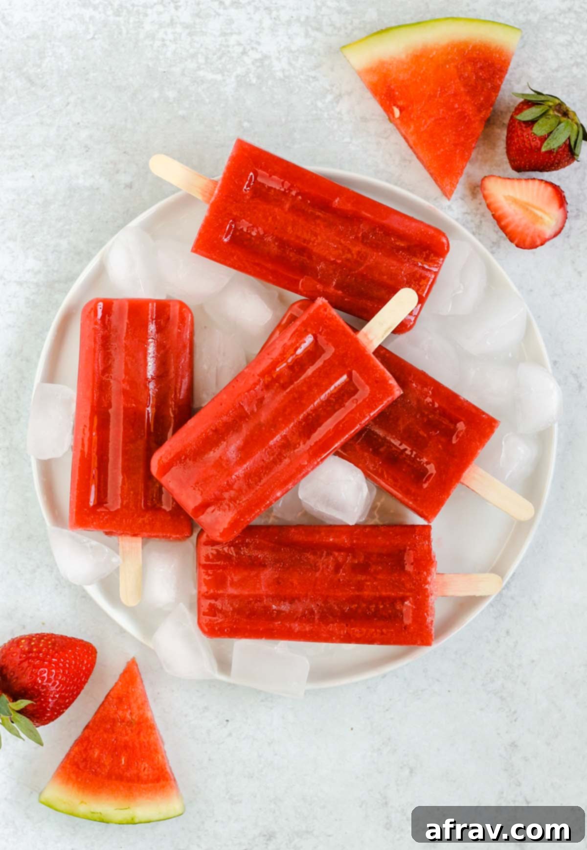 Simple 2-Ingredient Strawberry Watermelon Popsicles 5 strawberry watermelon popsicles on a round white plate with ice cubes