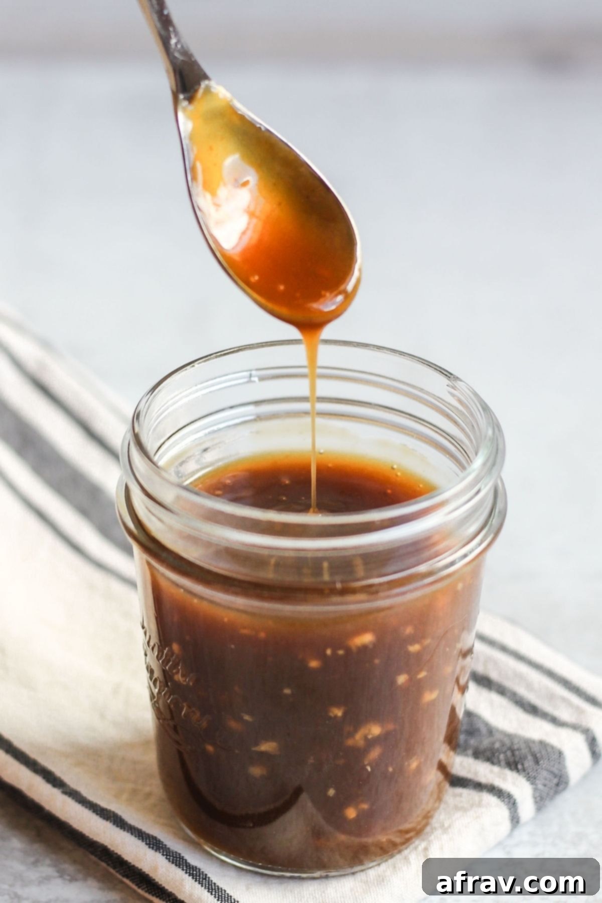 Teriyaki sauce dripping from a spoon over a mason jar filled with teriya