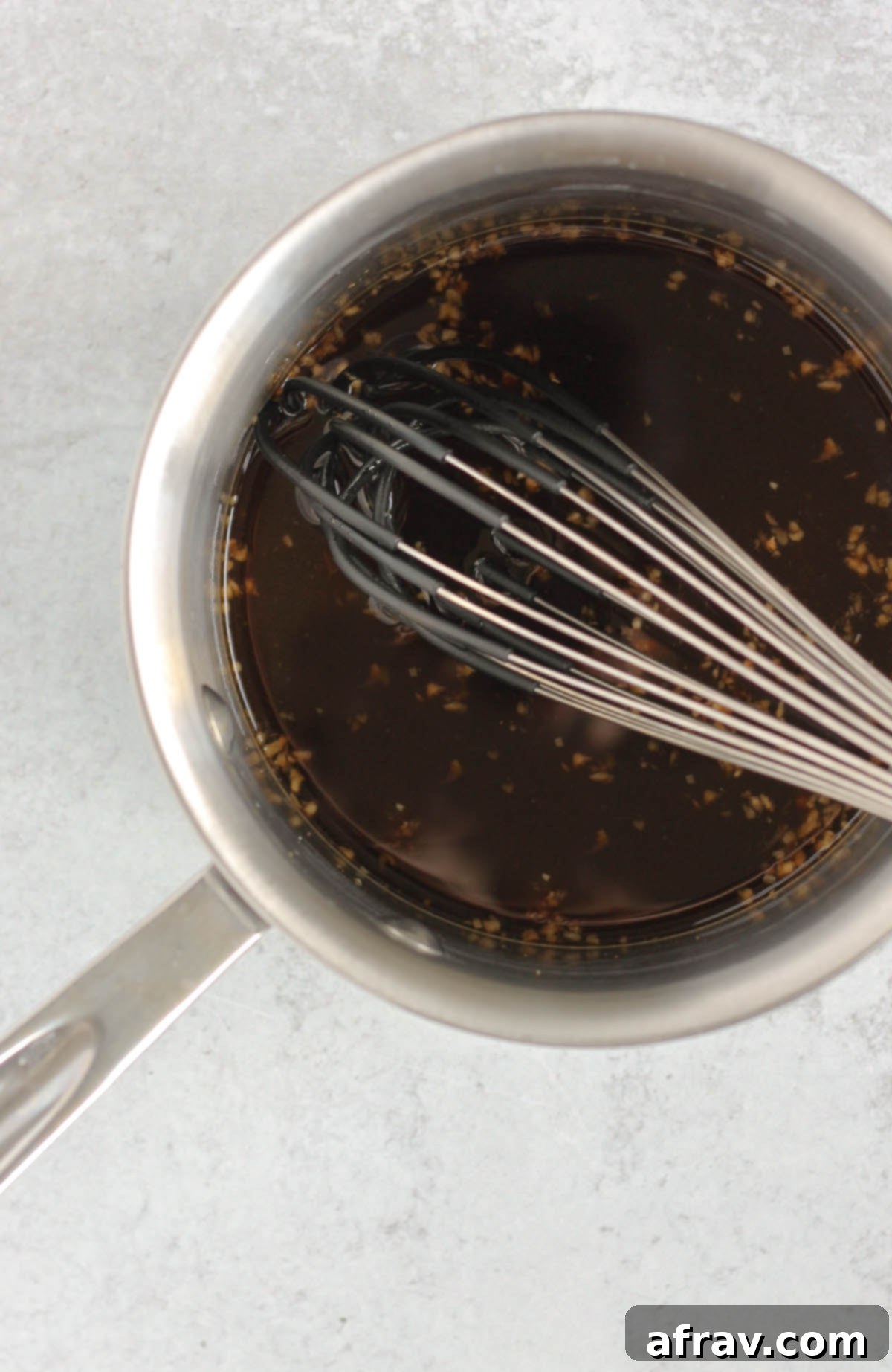 A whisk in a sauce pan filled with teriyaki sauce ingredients.