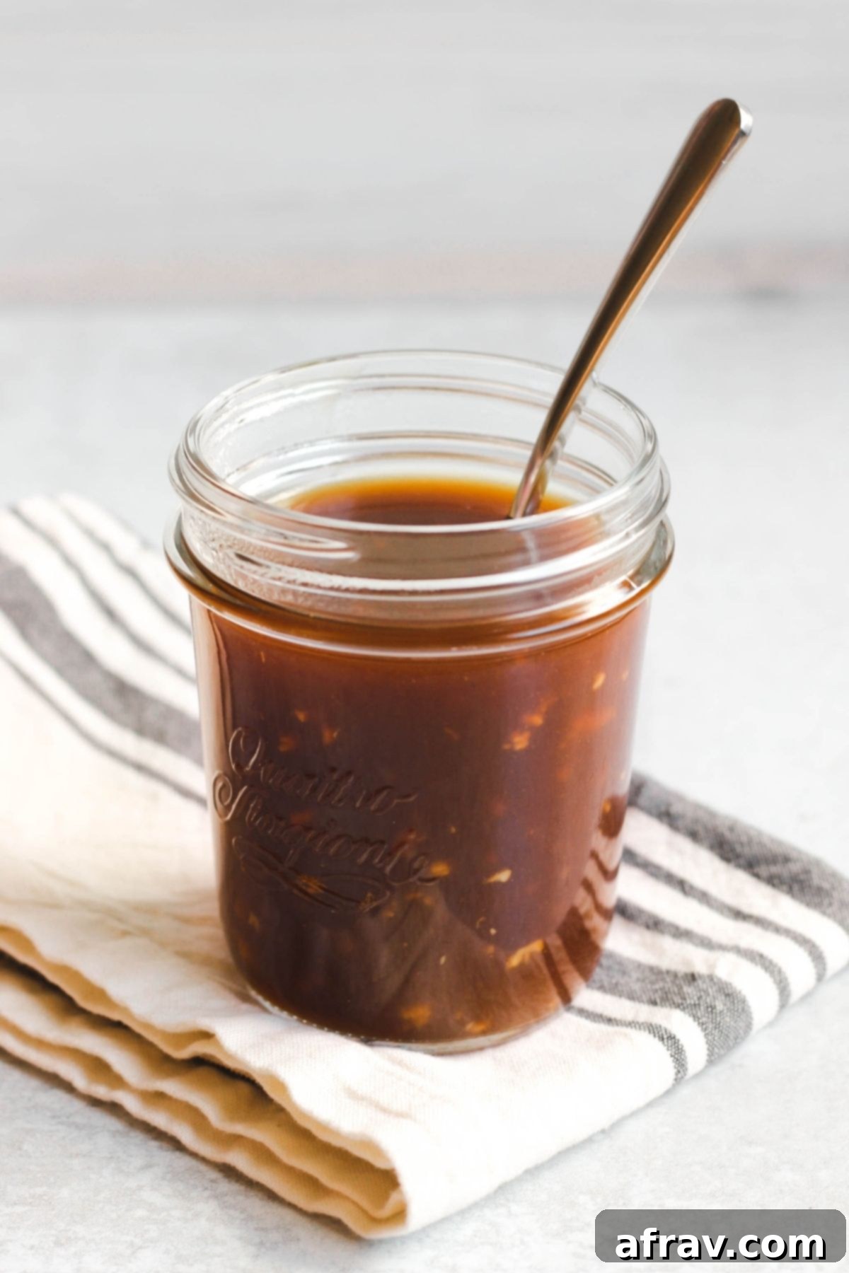 A spoon in a mason jar filled with teriyaki sauce.