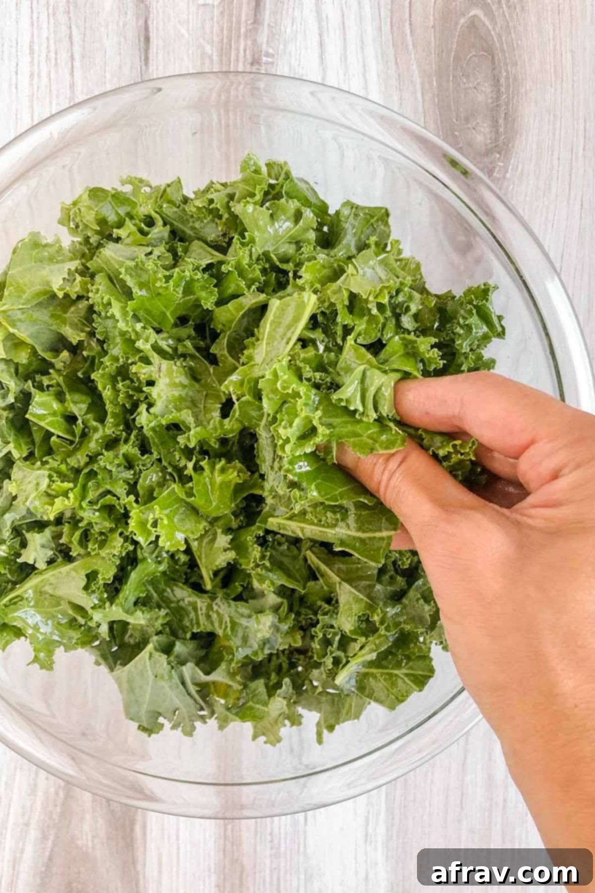 Hand massaging kale leaves in a glass mixing bowl.