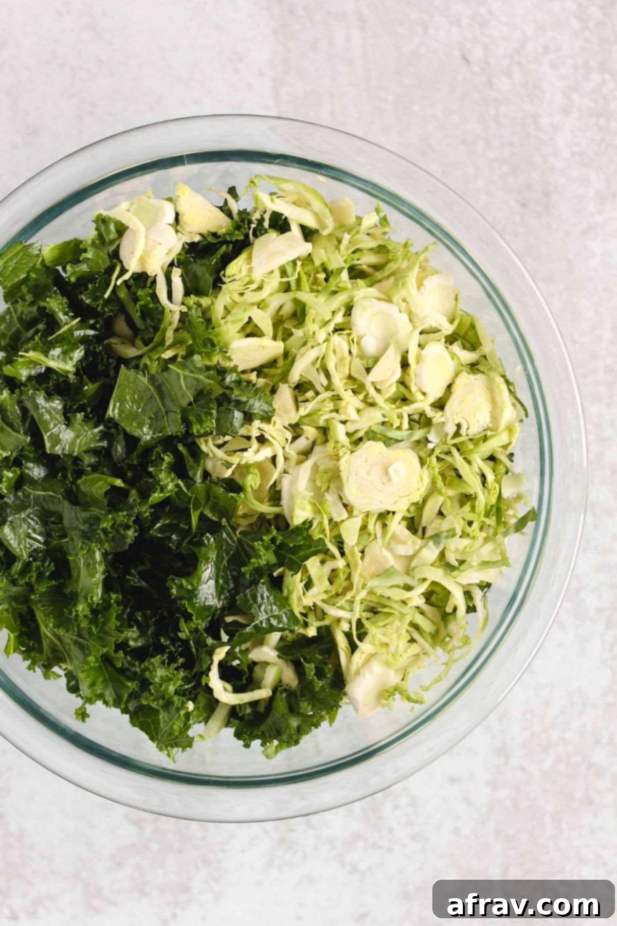 Shaved Brussels sprouts and kale leaves in a glass mixing bowl.