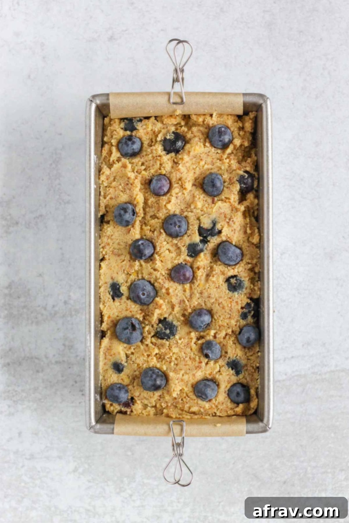 Zesty Lemon Blueberry Almond Loaf 7 Almond flour blueberry bread batter spread evenly in a parchment-lined loaf pan, with extra blueberries on top.
