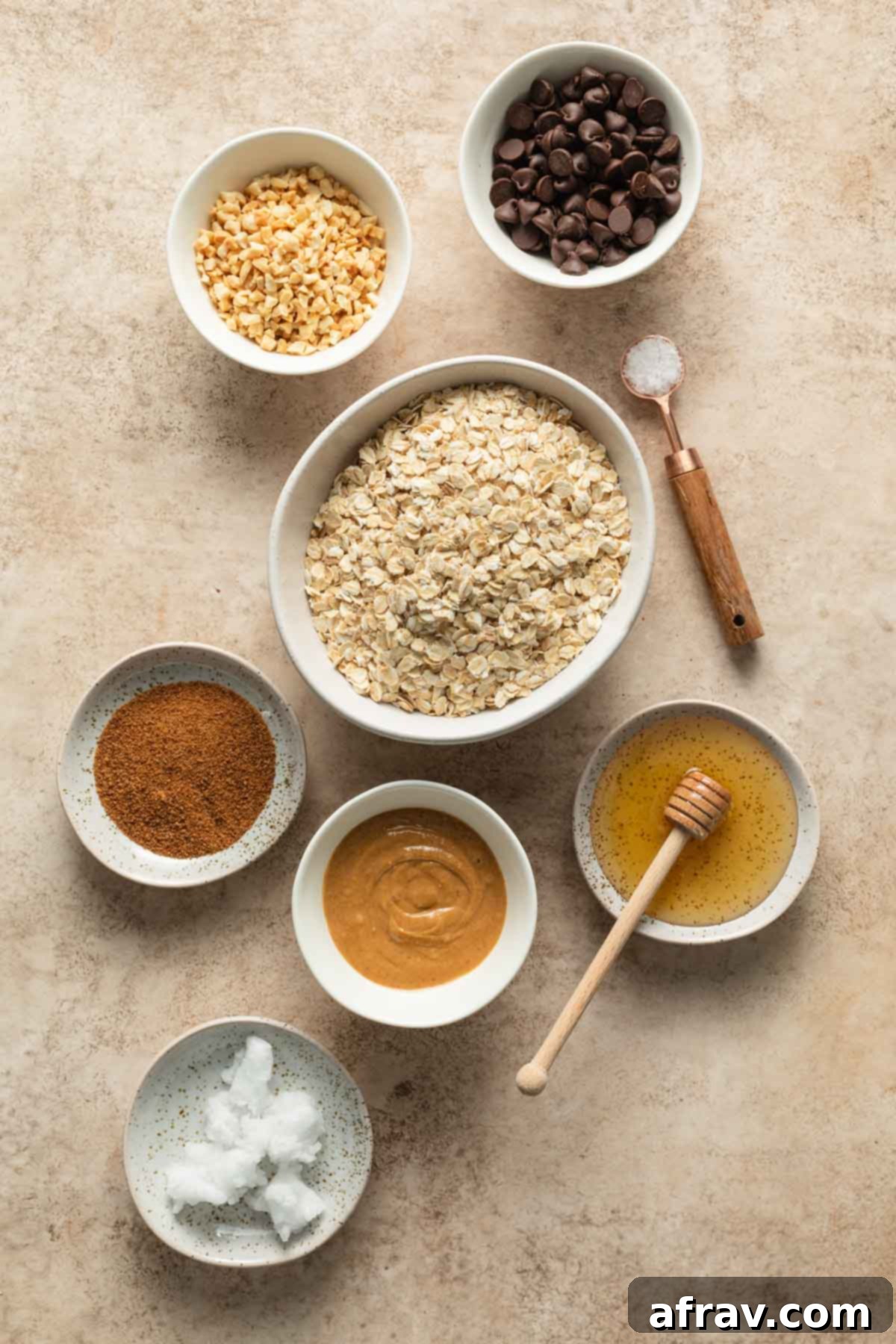 Various raw ingredients for peanut butter granola, including oats, peanuts, peanut butter, honey, and chocolate chips, neatly arranged.
