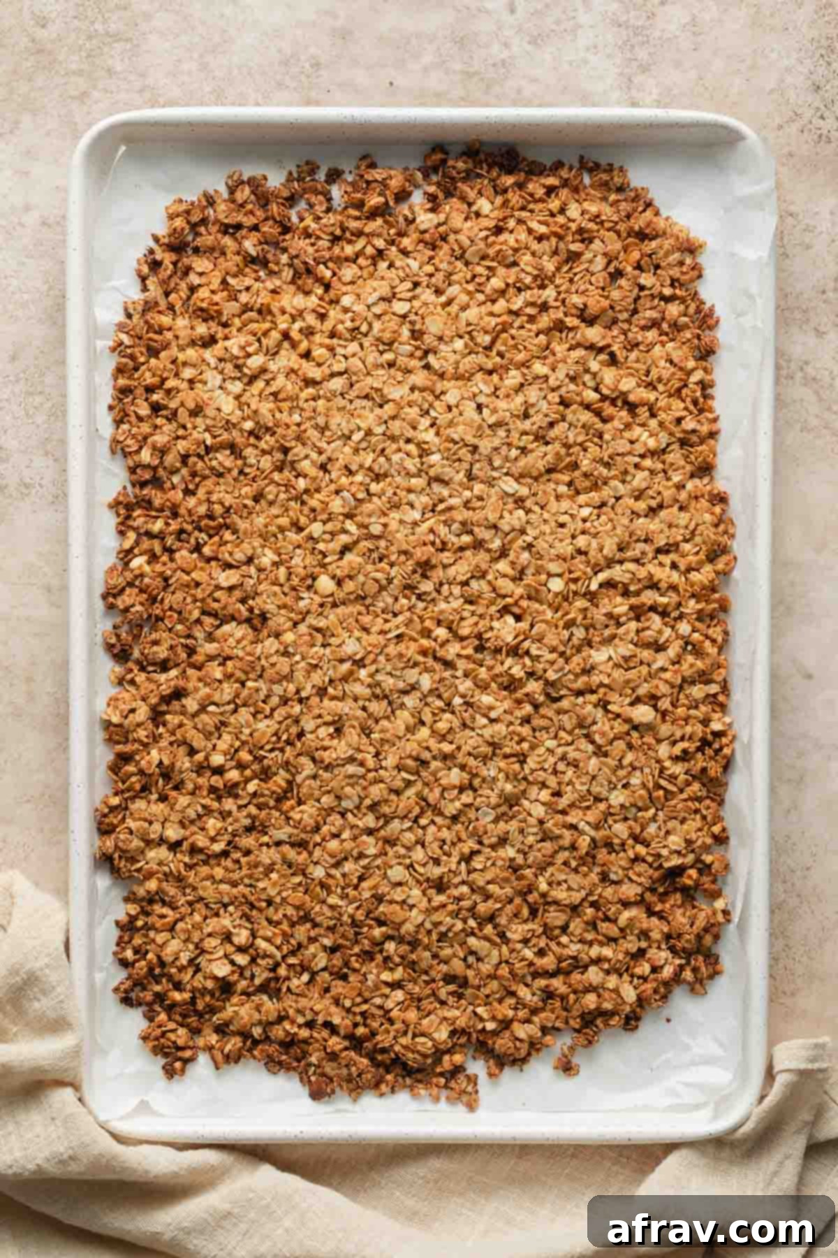 Freshly baked granola, golden-brown and still warm, cooling undisturbed on the baking sheet.