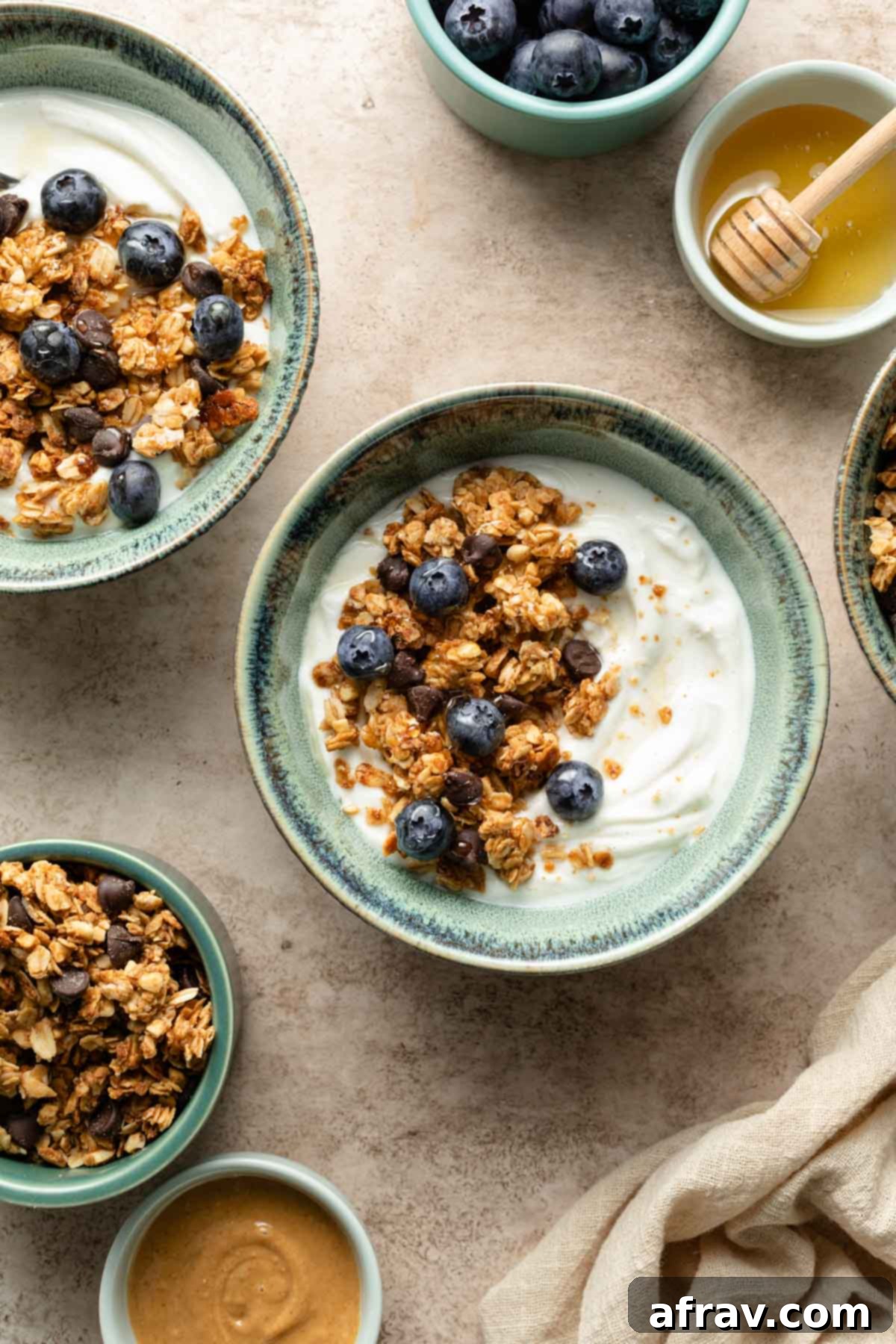 Overhead view of two green bowls filled with creamy yogurt, topped with homemade peanut butter granola and scattered fresh blueberries.