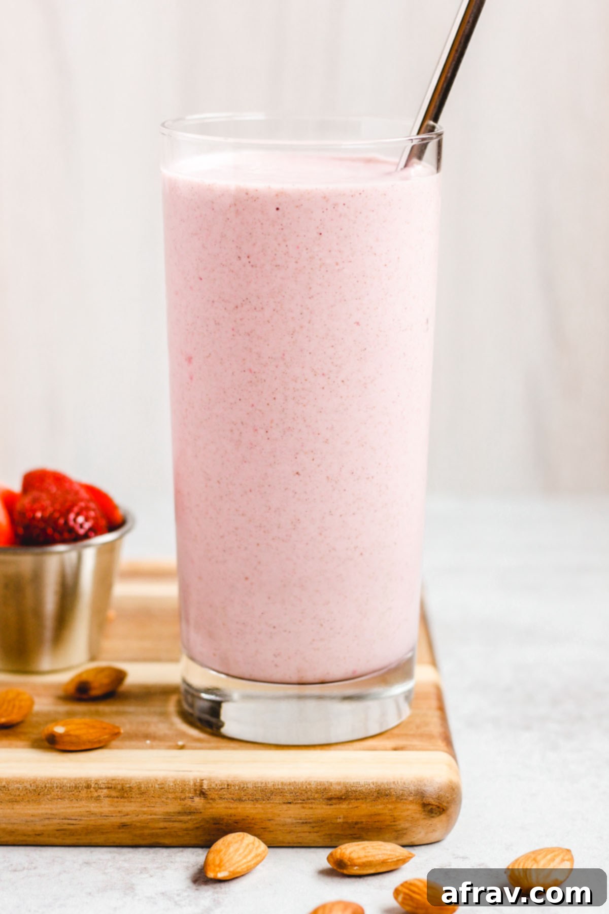 side view of strawberry almond smoothie in a tall glass with stainless steel straw