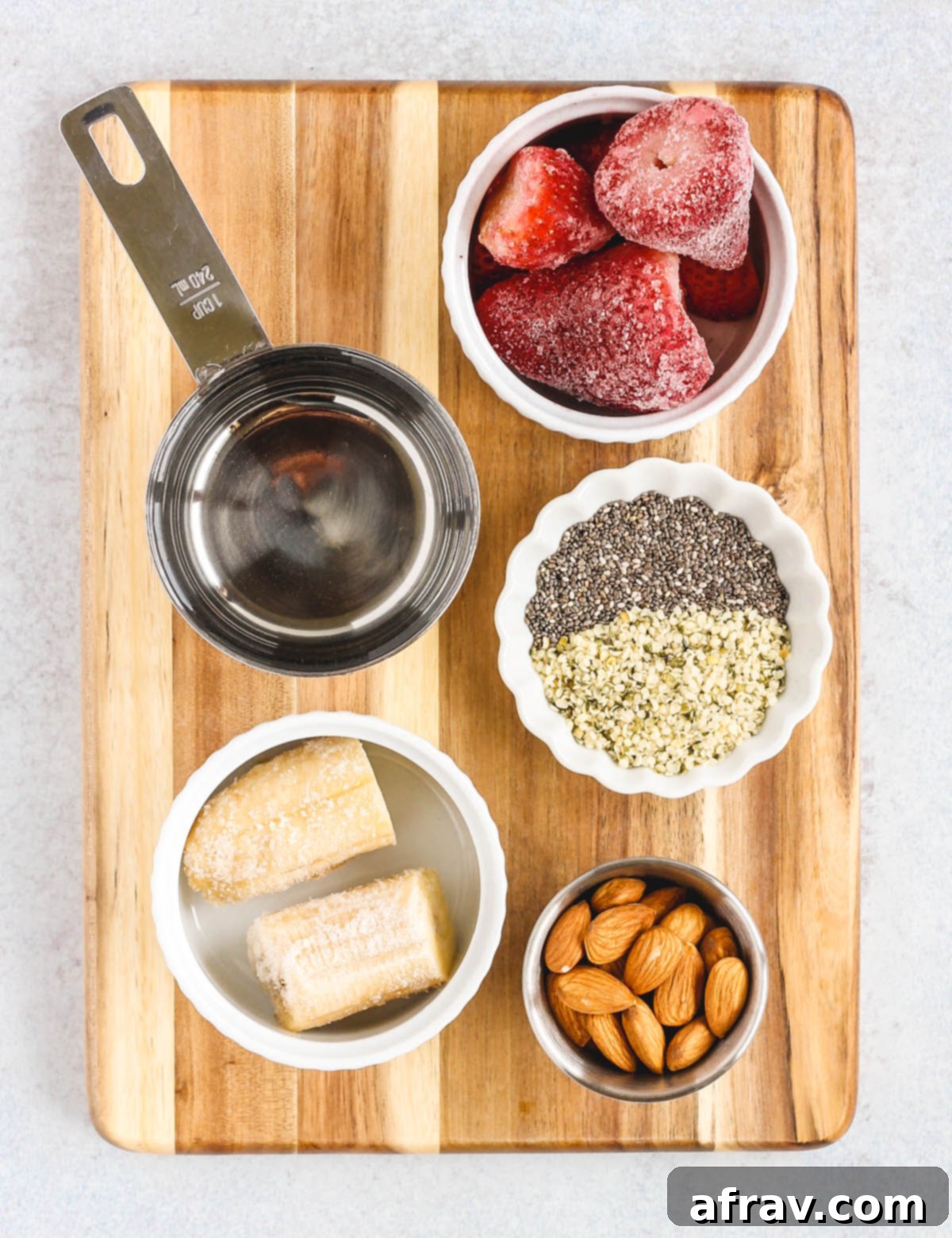 strawberry almond smoothie ingredients portioned out in little bowls sitting on a wood cutting board
