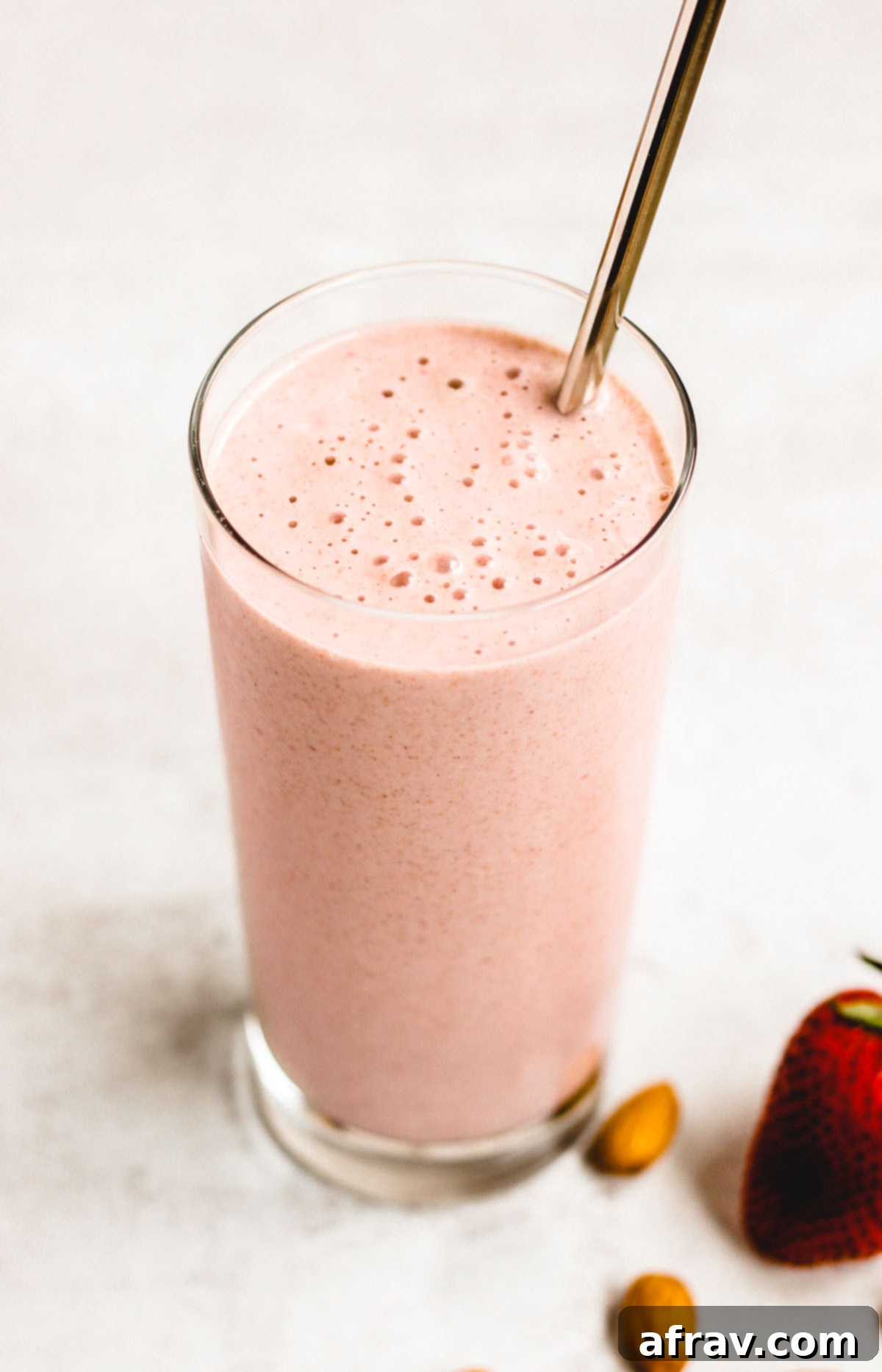 side angle view of strawberry almond smoothie in a glass with a stainless steel straw