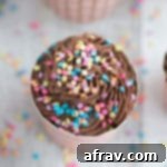 Overhead view of Flourless Ricotta Cupcakes topped with Chocolate Coconut Cream and sprinkles on a white wooden surface.