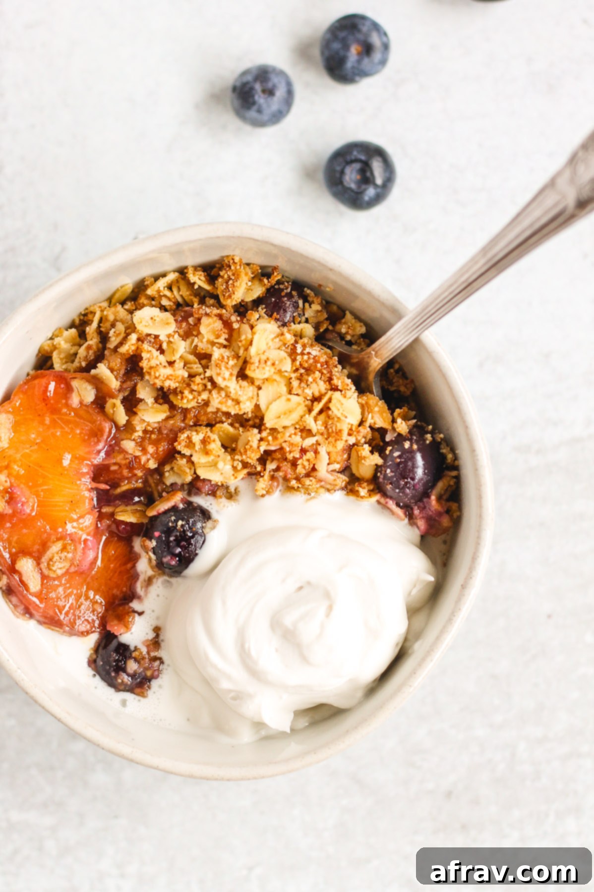 small bowl with spoon filled with peach crisp topped with coconut cream