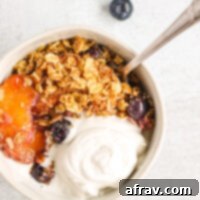 overhead view of peach and blueberry crisp in white bowl topped with coconut whipped cream