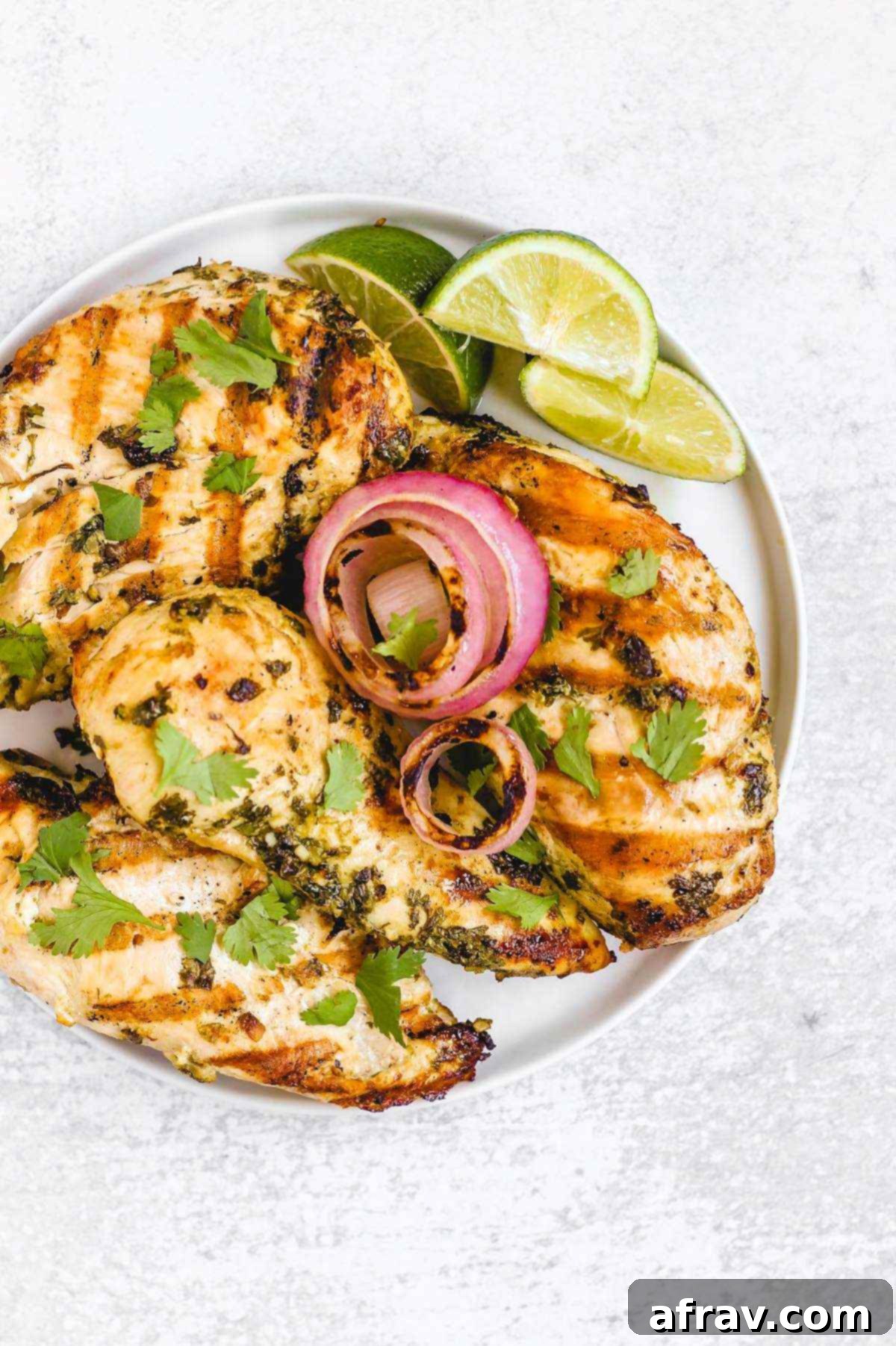 Zesty Cilantro Lime Chicken 2 Four perfectly grilled cilantro lime chicken breasts, garnished with grilled onions and fresh lime slices, beautifully arranged on a round plate.