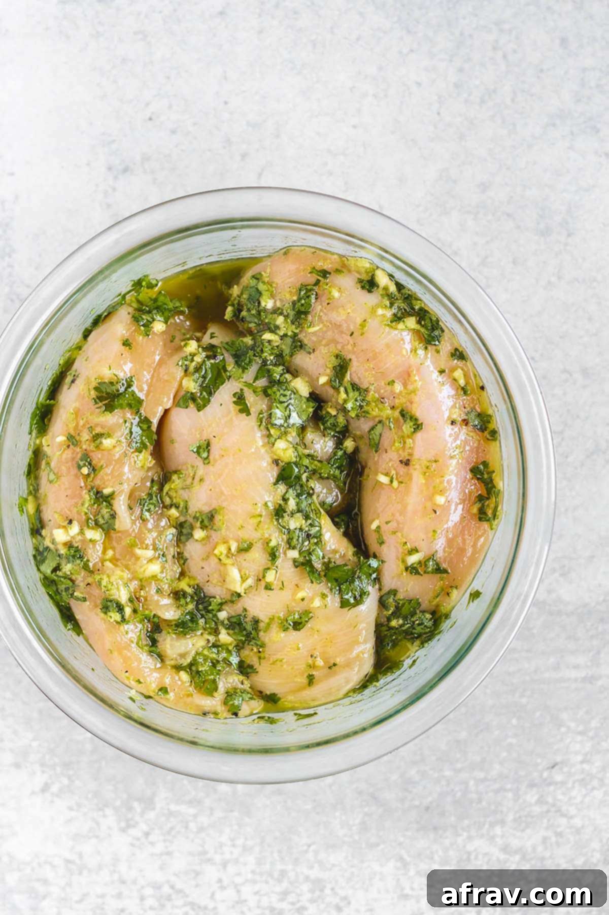 Zesty Cilantro Lime Chicken 4 Raw chicken breasts submerged in a vibrant green cilantro lime marinade within a clear glass mixing bowl, showcasing the fresh ingredients.