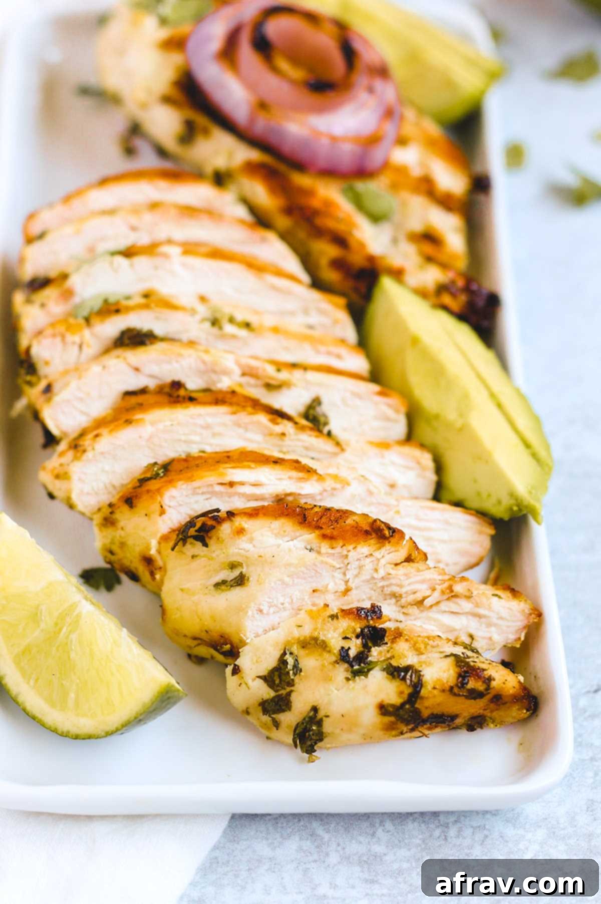 Zesty Cilantro Lime Chicken 5 A perfectly cooked and sliced cilantro lime chicken breast arranged on a rectangular plate, accompanied by a fresh lime wedge and creamy sliced avocado.