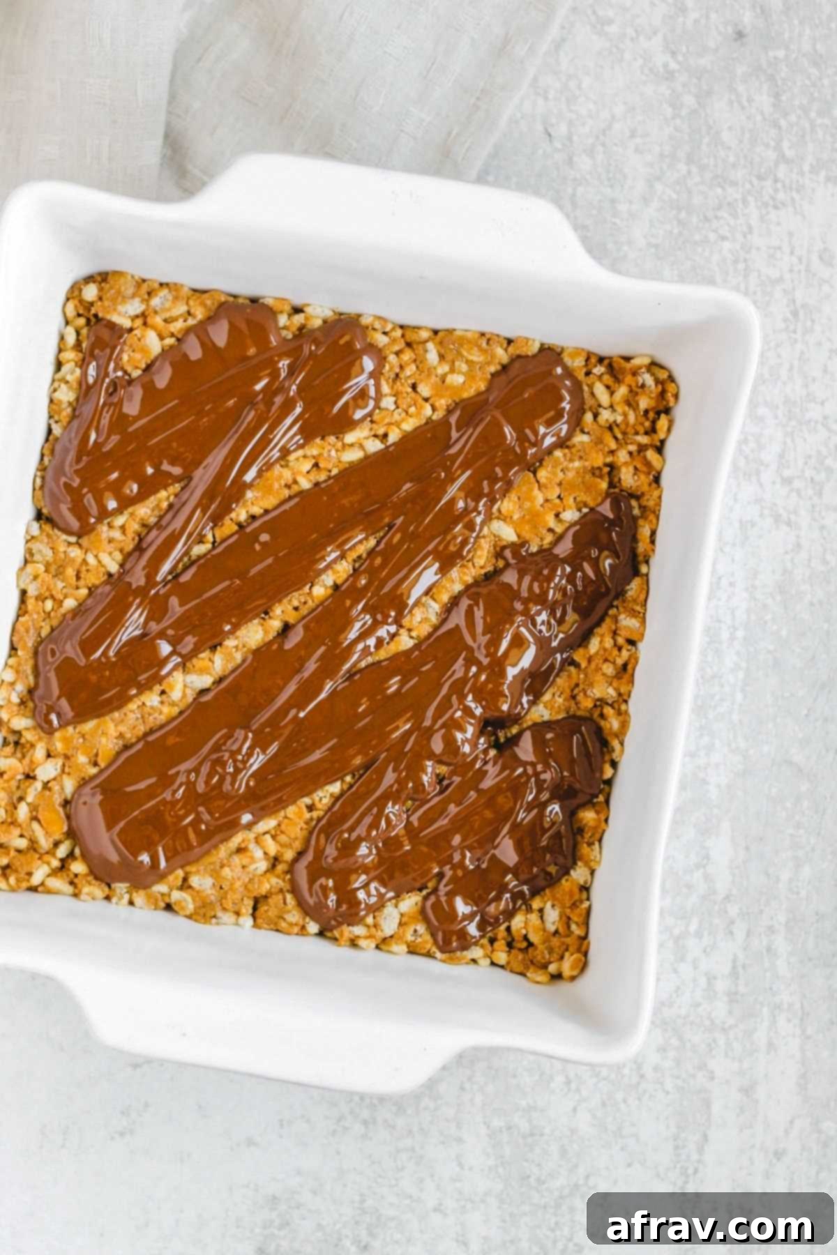 Peanut butter crispy bars in a square dish with chocolate drizzled on top.
