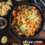 Loaded Veggie Nachos in a cast iron pan surrounded by dips, chips and beer on a wooden table.