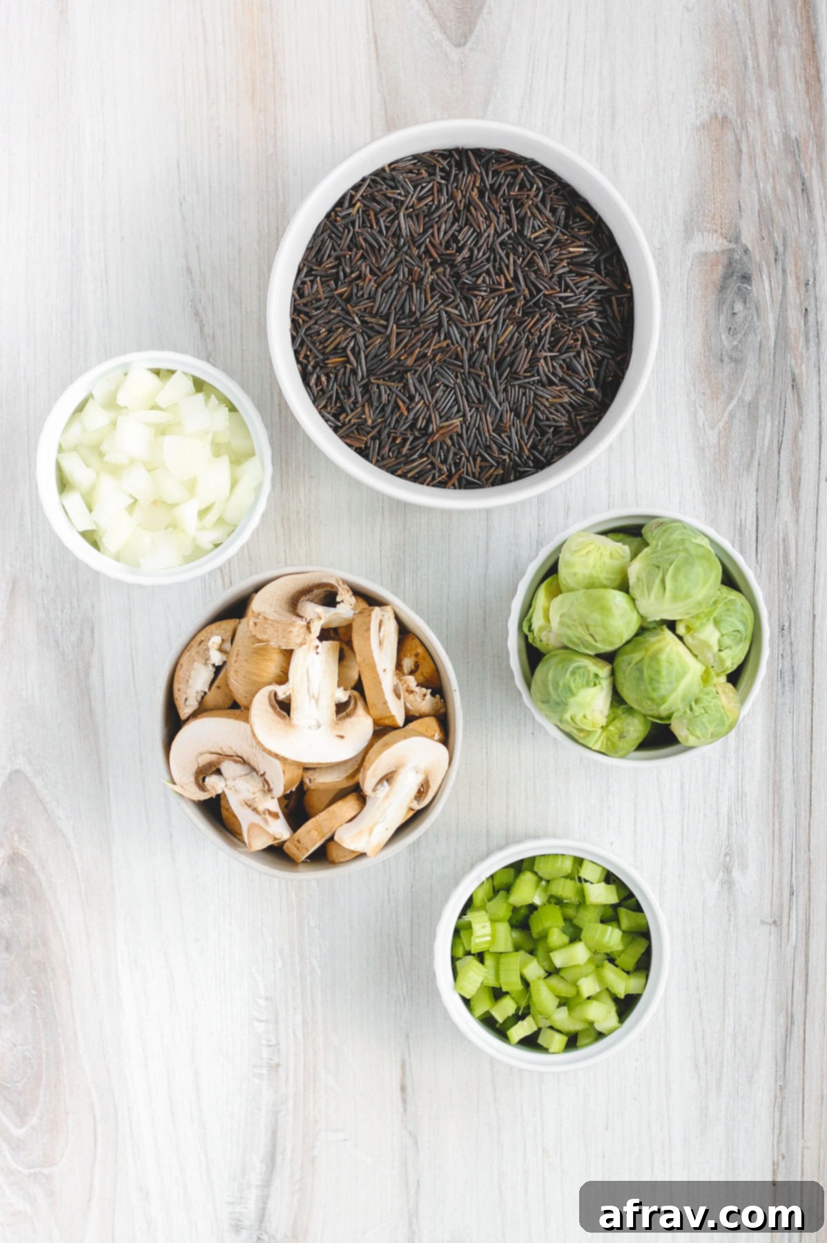 Slow-Cooked Wild Rice Delight 4 Bowl of prepped vegetables for wild rice pilaf: neatly sliced Brussels sprouts, mushrooms, chopped yellow onion, celery, and garlic cloves