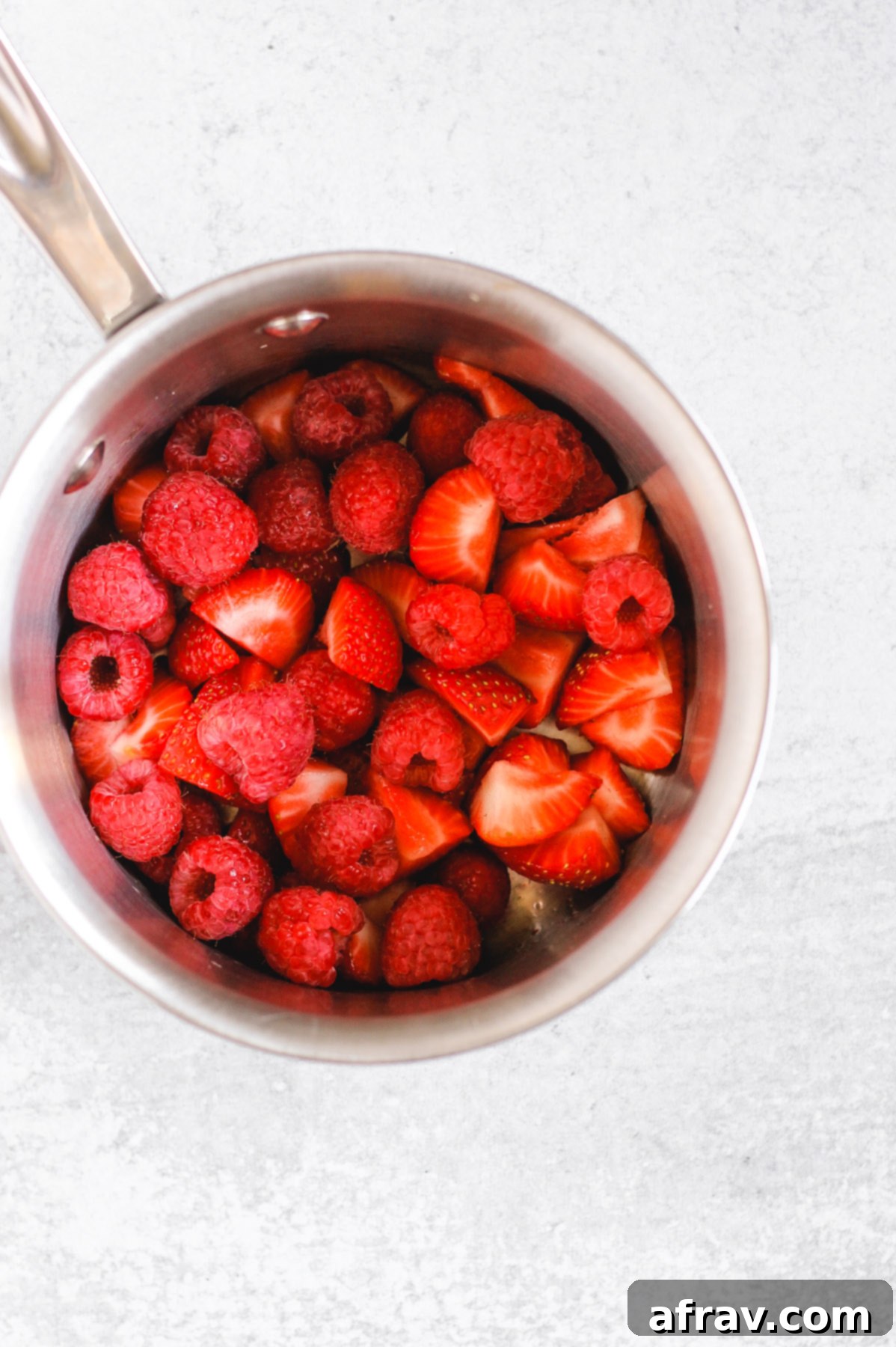 overhead view of sliced strawberries and raspberrries in stainless steal sauce pan