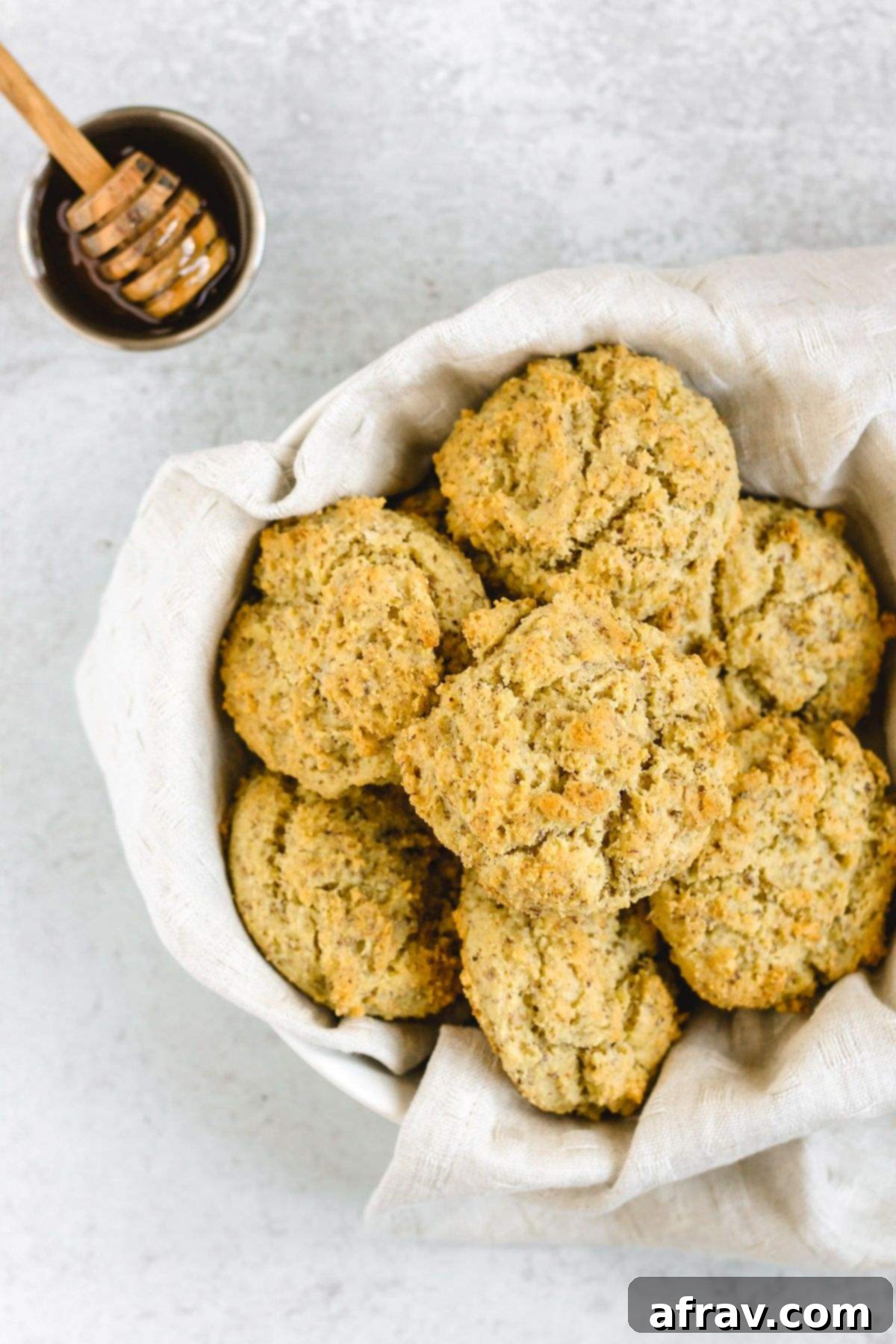 Fluffy Paleo Almond Flour Biscuits 2 Almond flour drop biscuits in a round bread basket with a dish of honey on the side, showcasing their golden-brown perfection.