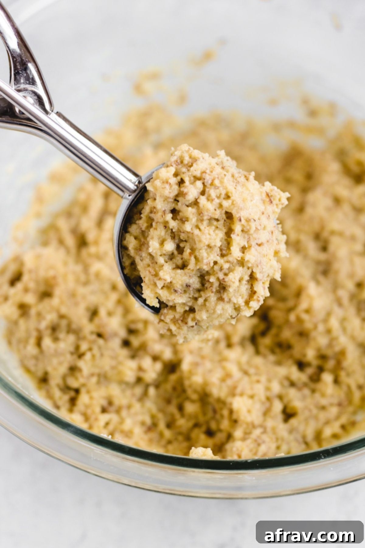 Fluffy Paleo Almond Flour Biscuits 6 Spring loaded cookie scoop scooping out almond flour biscuit dough from a glass mixing bowl onto a baking sheet.