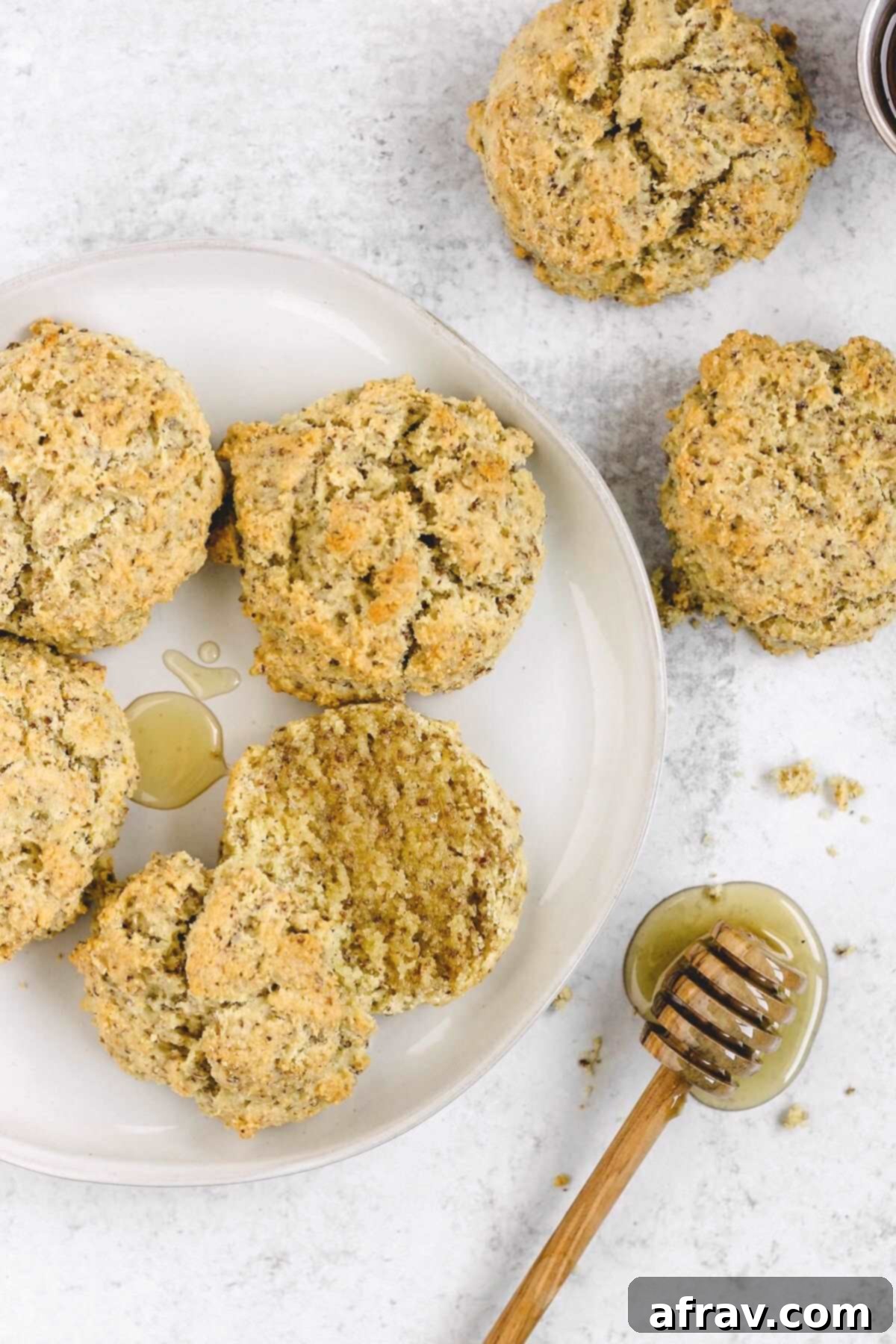 Fluffy Paleo Almond Flour Biscuits 9 Almond flour biscuits on a round plate with one cut open and drizzled with honey, a honey dipper on the side.