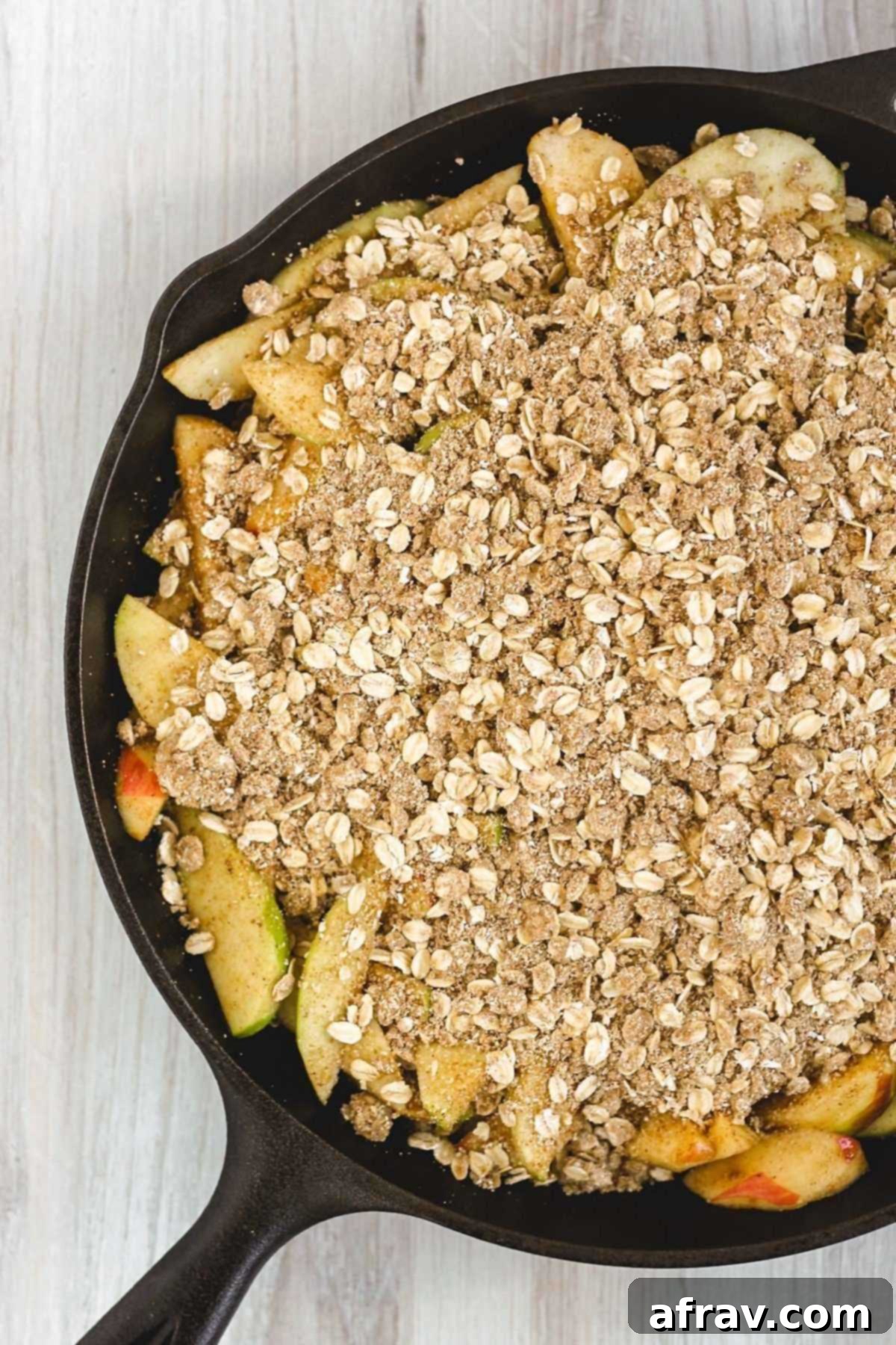 Wholesome Gluten-Free Apple Crisp Made Easy 5 Sliced apples topped with oat crumble in a cast iron skillet, ready to be baked.