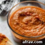 Homemade marinara sauce in a glass bowl next to a wooden spoon with sauce on it.