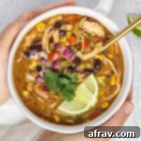 Hands holding a bowl of chicken chili topped with fresh cilantro and a lime wedge.