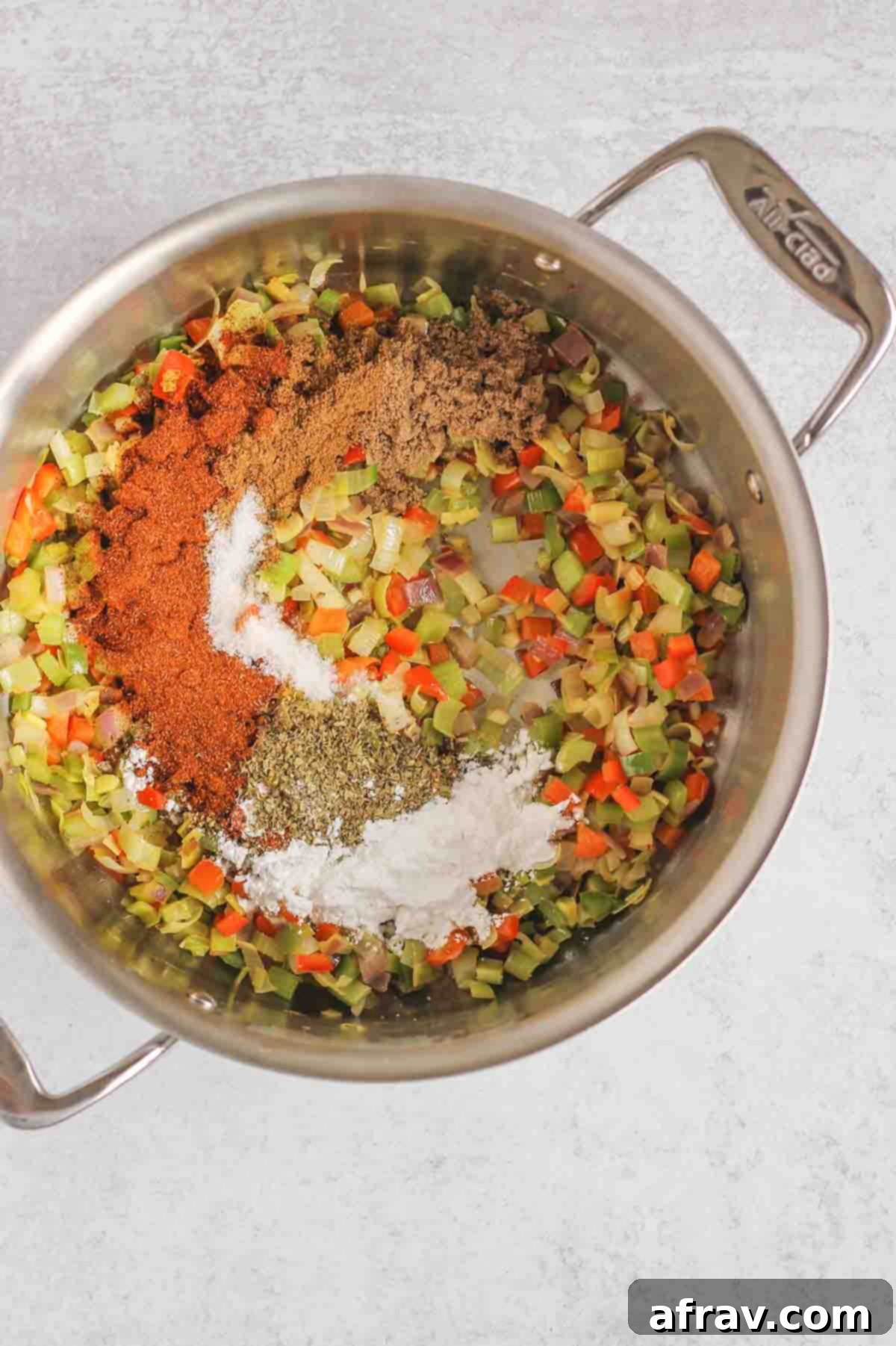 Sauteed aromatic vegetables and a rich blend of seasonings in a large stainless steel stock pot, forming the flavor base of the chili.