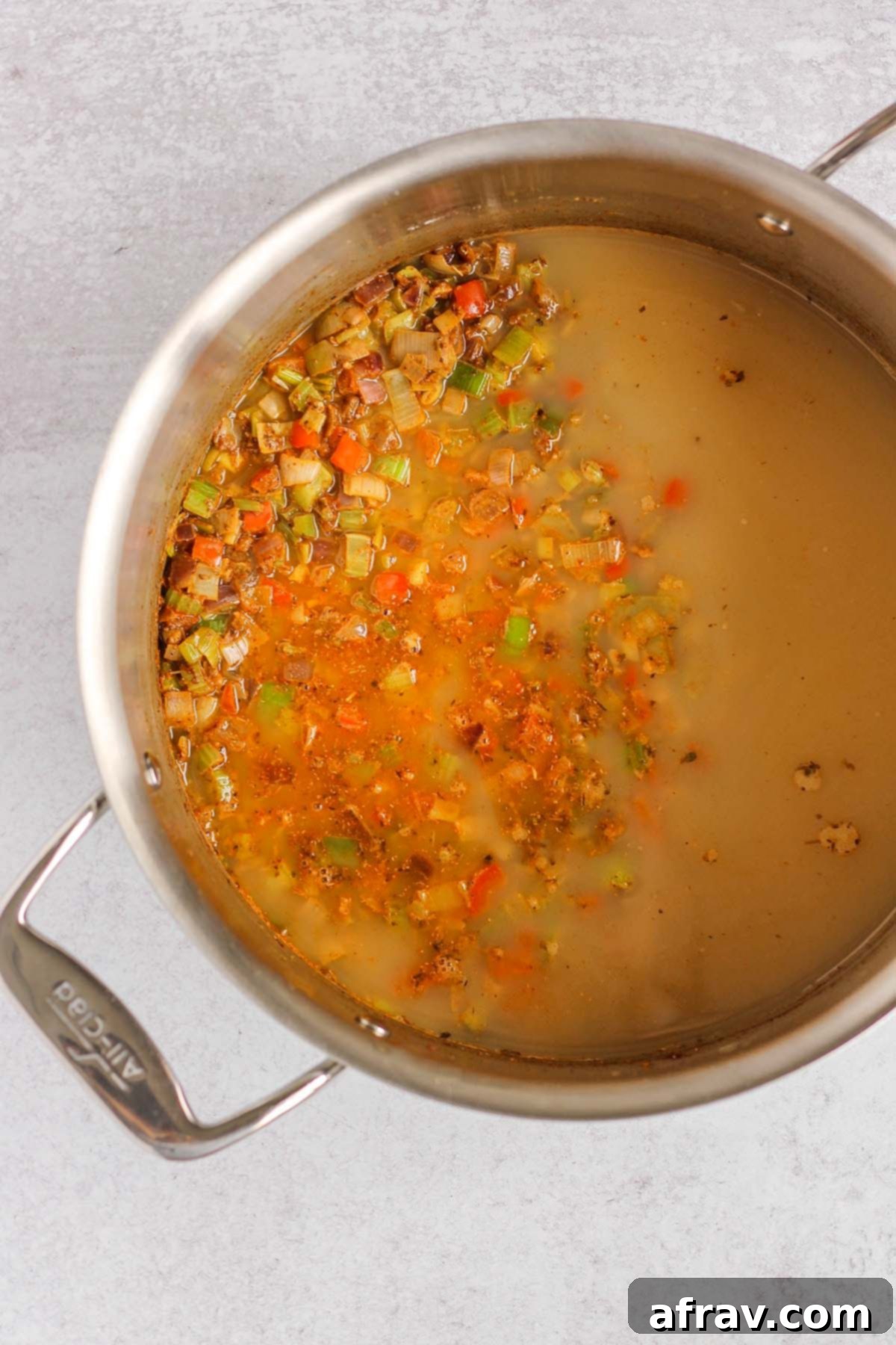 The savory base of sauteed vegetables and spices with chicken bone broth added, simmering in a stainless steel pot.