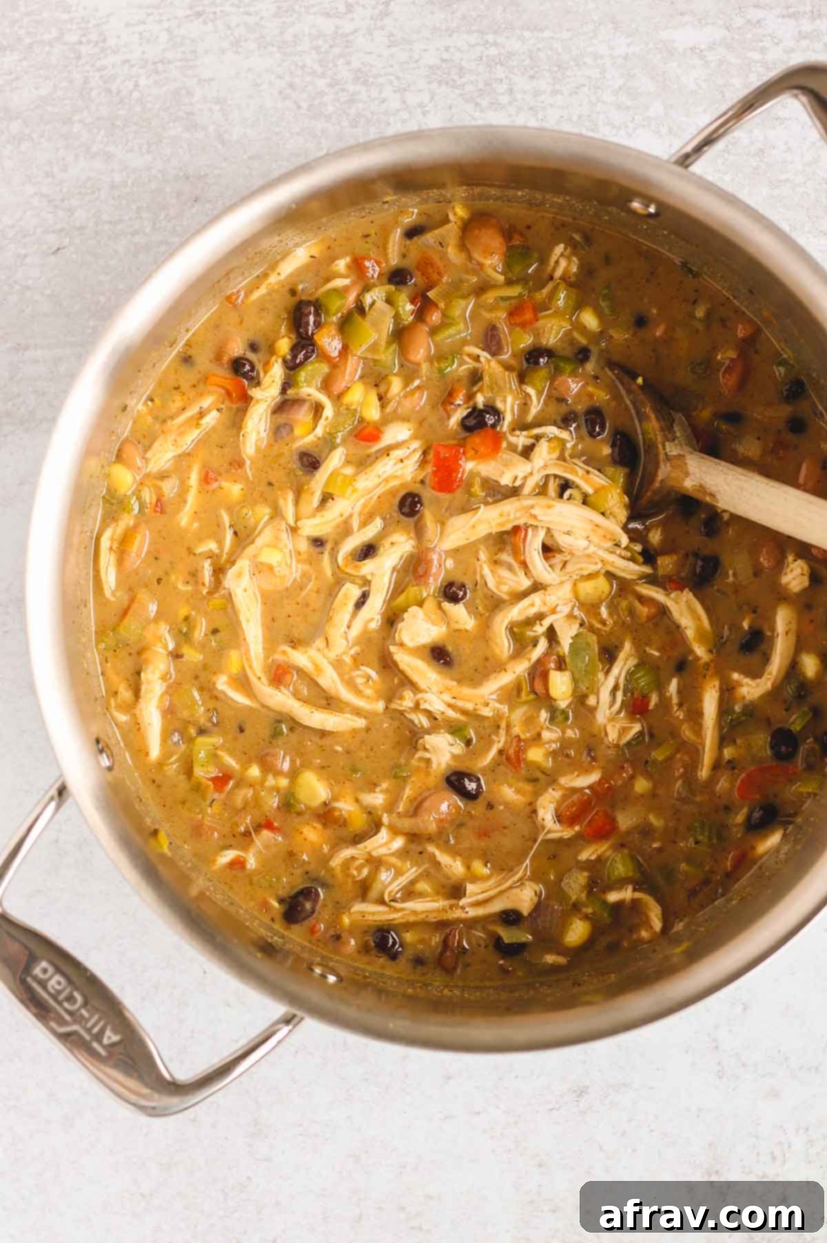 A wooden spoon stirring a fully prepared Southwest Chicken Chili in a stainless steel pot, ready for serving.