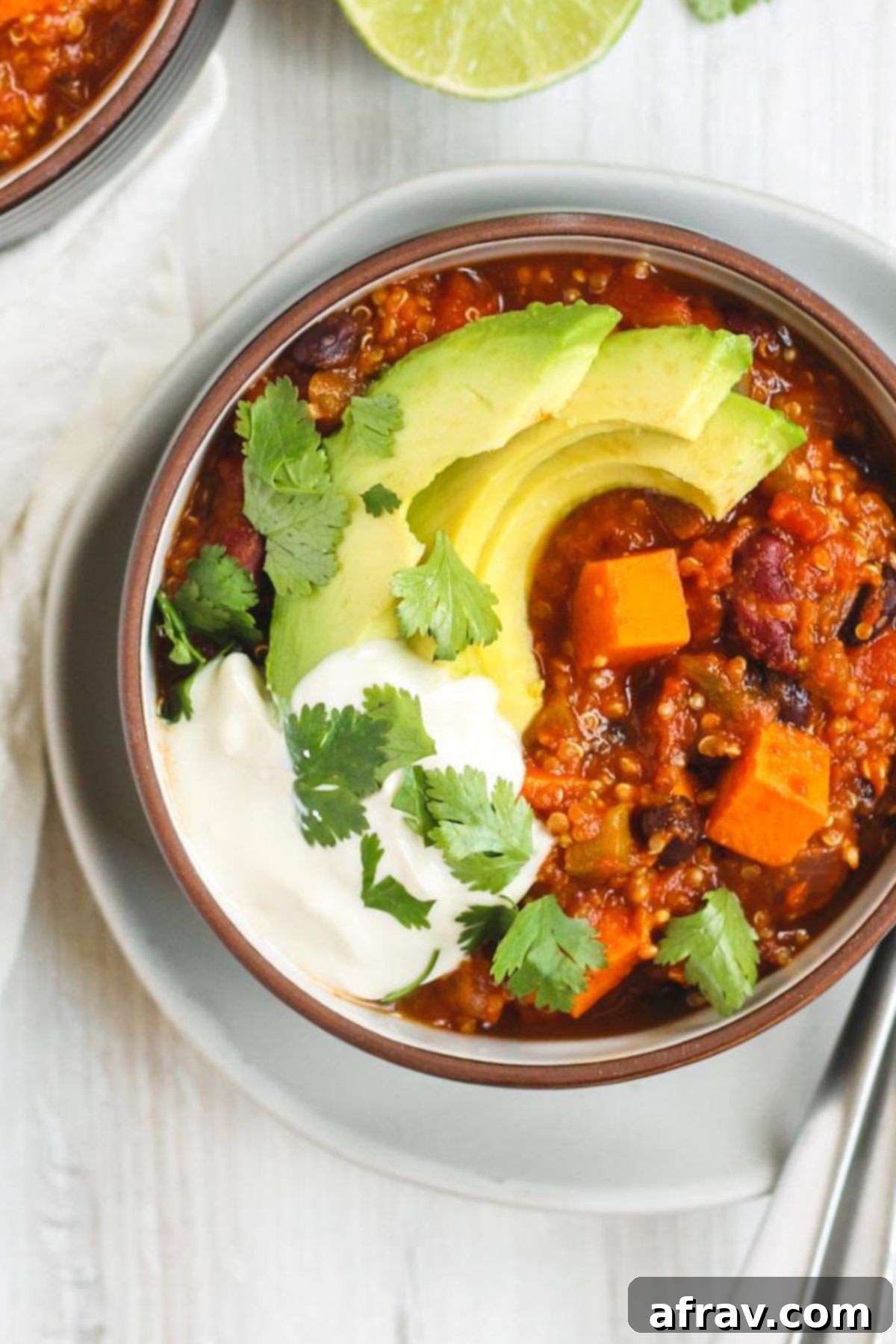 Hearty Vegan Sweet Potato Chili 2 Vegetarian sweet potato topped with avocado, cilantro, and sour cream in a dark bowl sitting on a white plate.