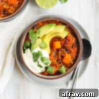 Hearty Vegan Sweet Potato Chili 7 Vegetarian sweet potato topped with avocado, cilantro, and sour cream in a dark bowl sitting on a white plate.