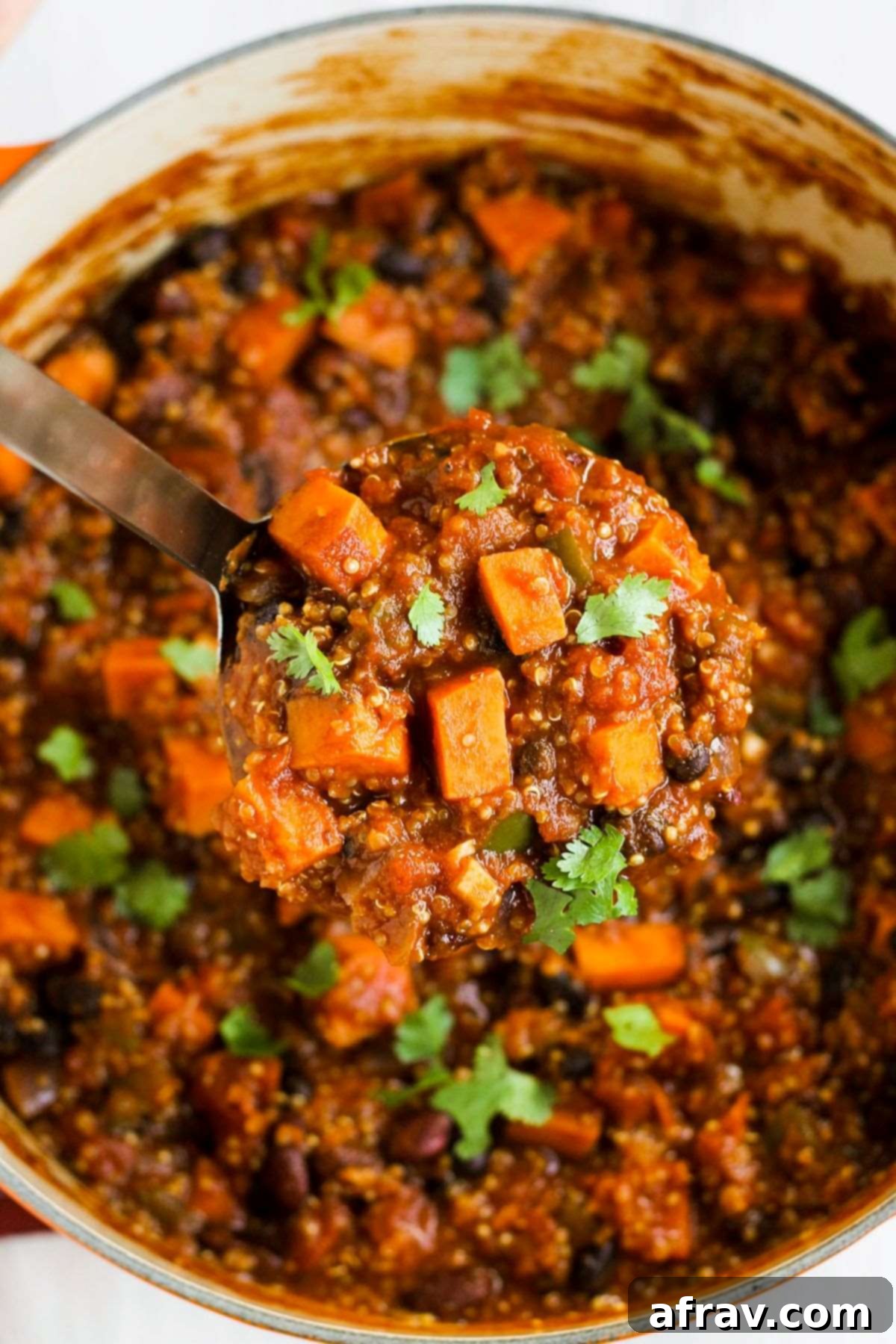Hearty Vegan Sweet Potato Chili 5 A stainless steel ladle scooping out a big scoop of sweet potato chili from a large stock pot.