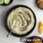Overhead view of creamy herb dip in a black bowl served with crackers, chips and cucumber.