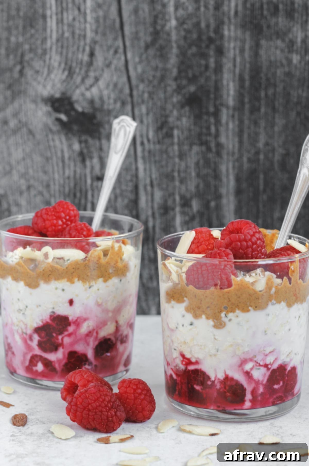 two glass cups filled with overnight oats, raspberries, almond butter, and almonds