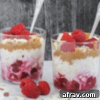 Two glass cups filled with layers of oats, raspberries, almond butter and almonds.