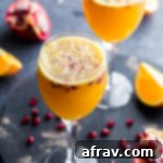 Two Ginger Beer Mimosas in wine glasses on a dark surface, surrounded by pomegranate arils. A festive, sparkling drink.