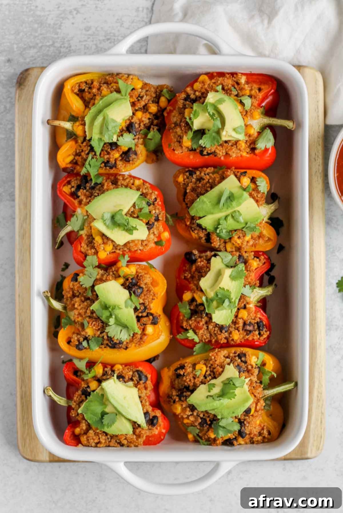 vegan stuffed peppers topped with avocado and cilantro in a white baking dish