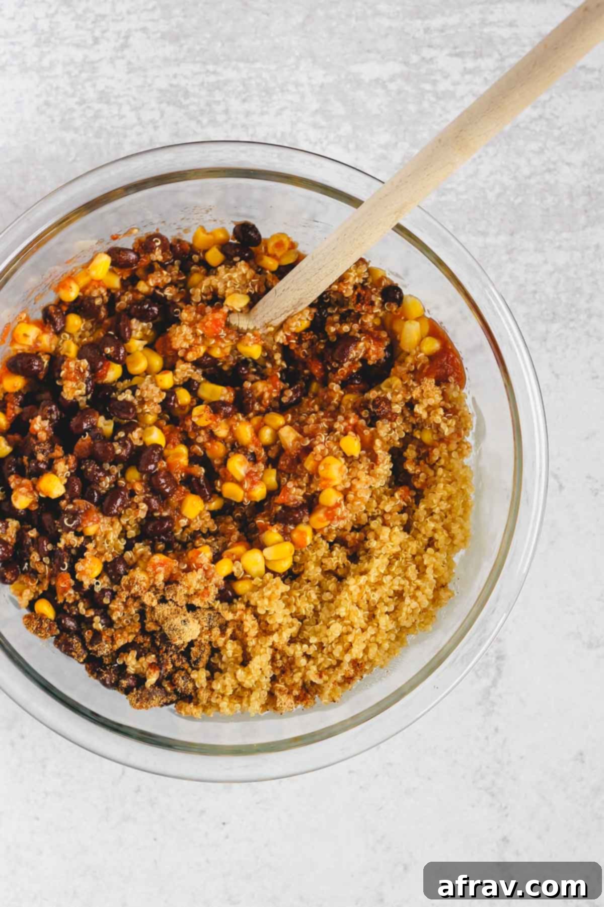 beans, corn, quinoa, salsal, spices mixed together in a glass mixing bowl