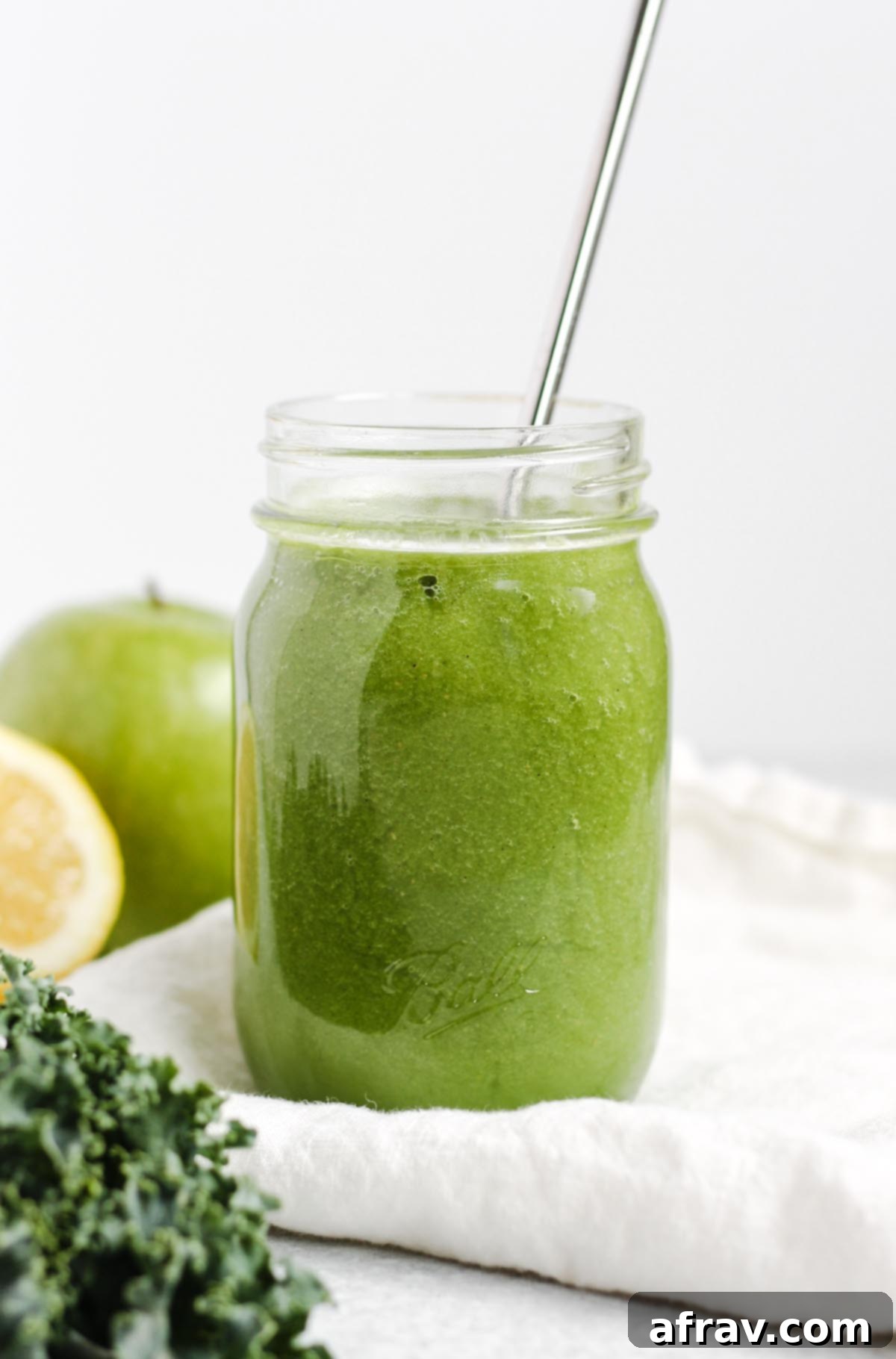 A vibrant green apple kiwi kale smoothie served in a mason jar with a reusable stainless steel straw, garnished with a fresh kiwi slice.