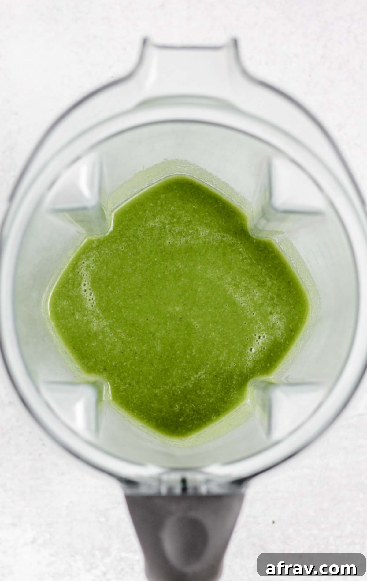 A high-speed blender container filled with a perfectly smooth, bright green smoothie, just after blending.