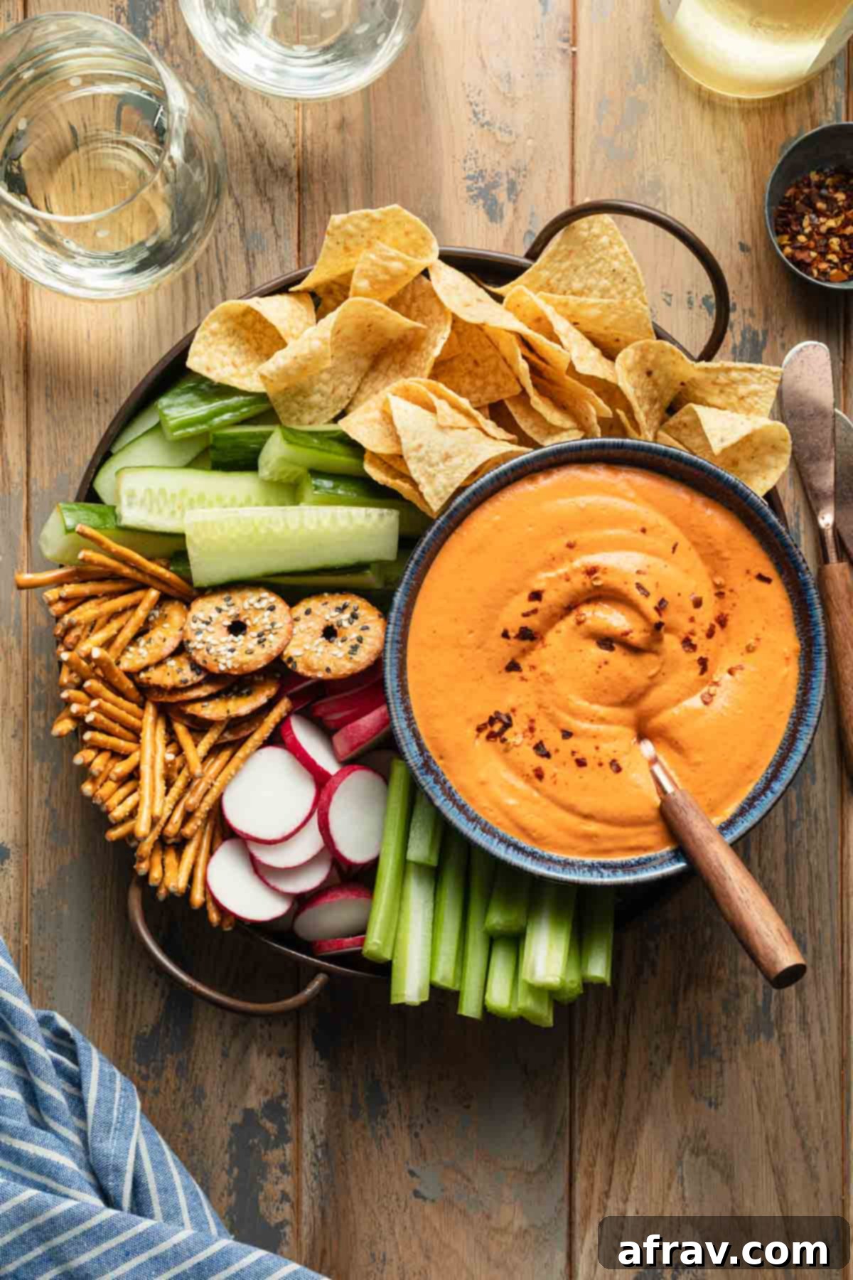 Overhead view of roasted red pepper dip served with a tray of fresh vegetables, crispy chips, and crunchy pretzels, highlighting its vibrant color and appealing texture.