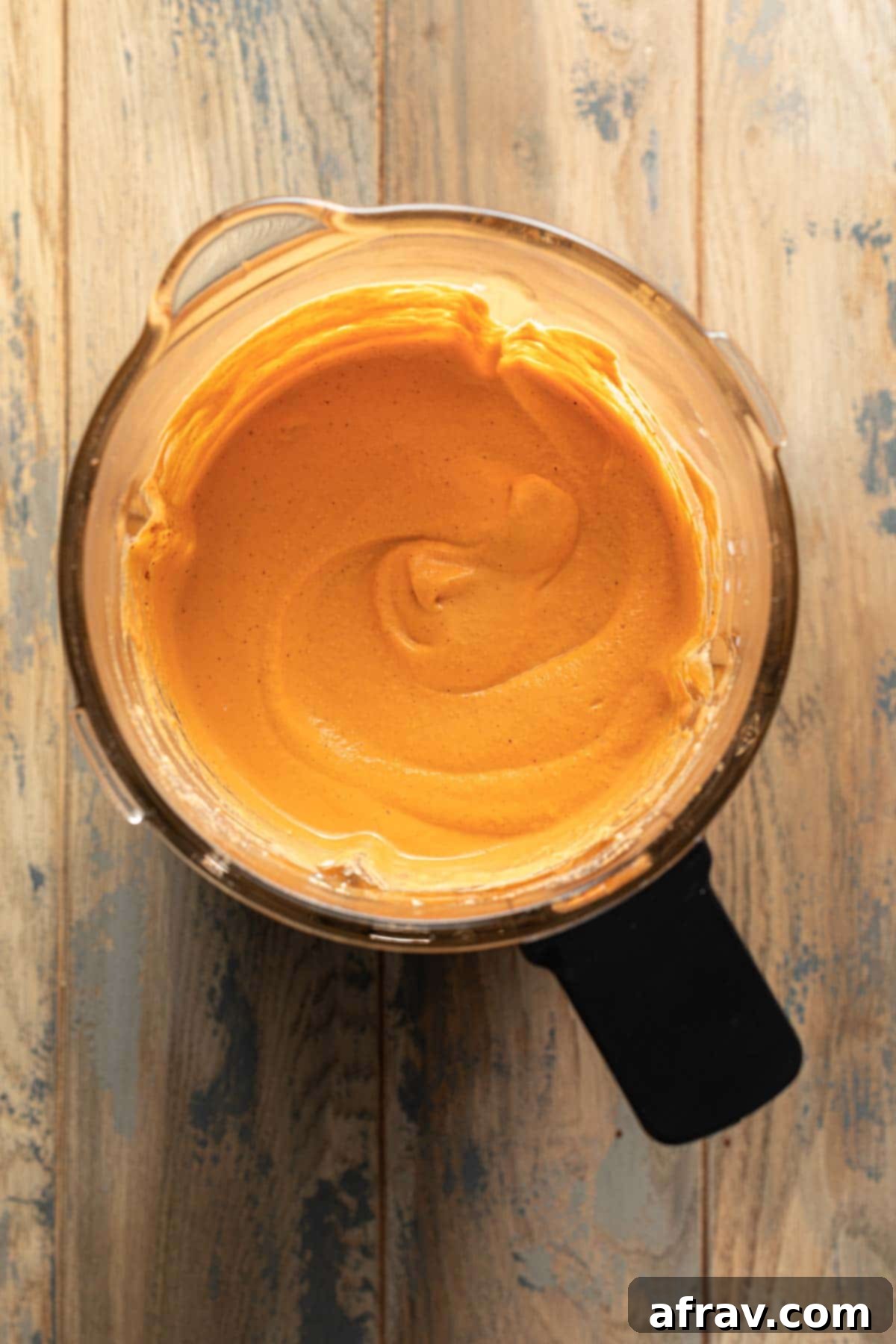 A high-powered blender jar filled with the vibrant, creamy roasted red pepper dip, showcasing its smooth and inviting texture during the blending process.