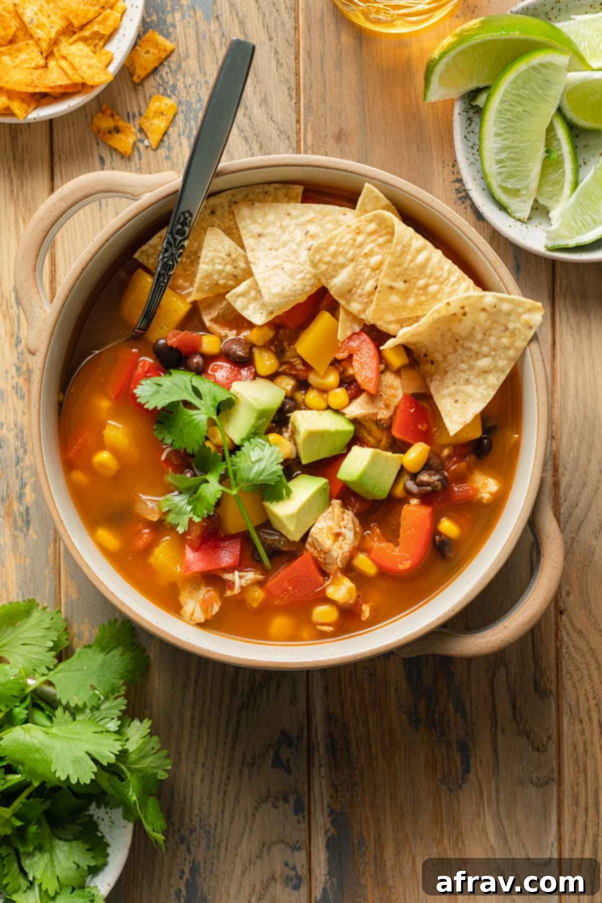 Overhead view of chicken fajita soup in a bowl next to cilantro and lime wedges.