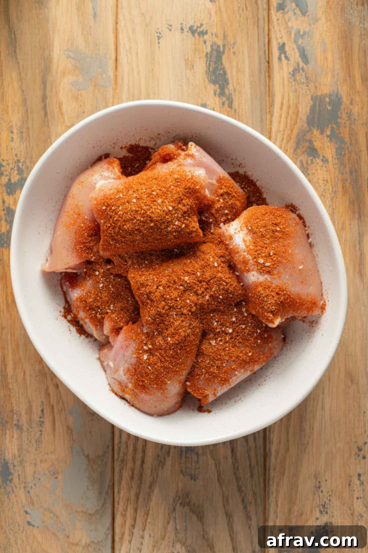 Seasoned chicken thighs in a white bowl.