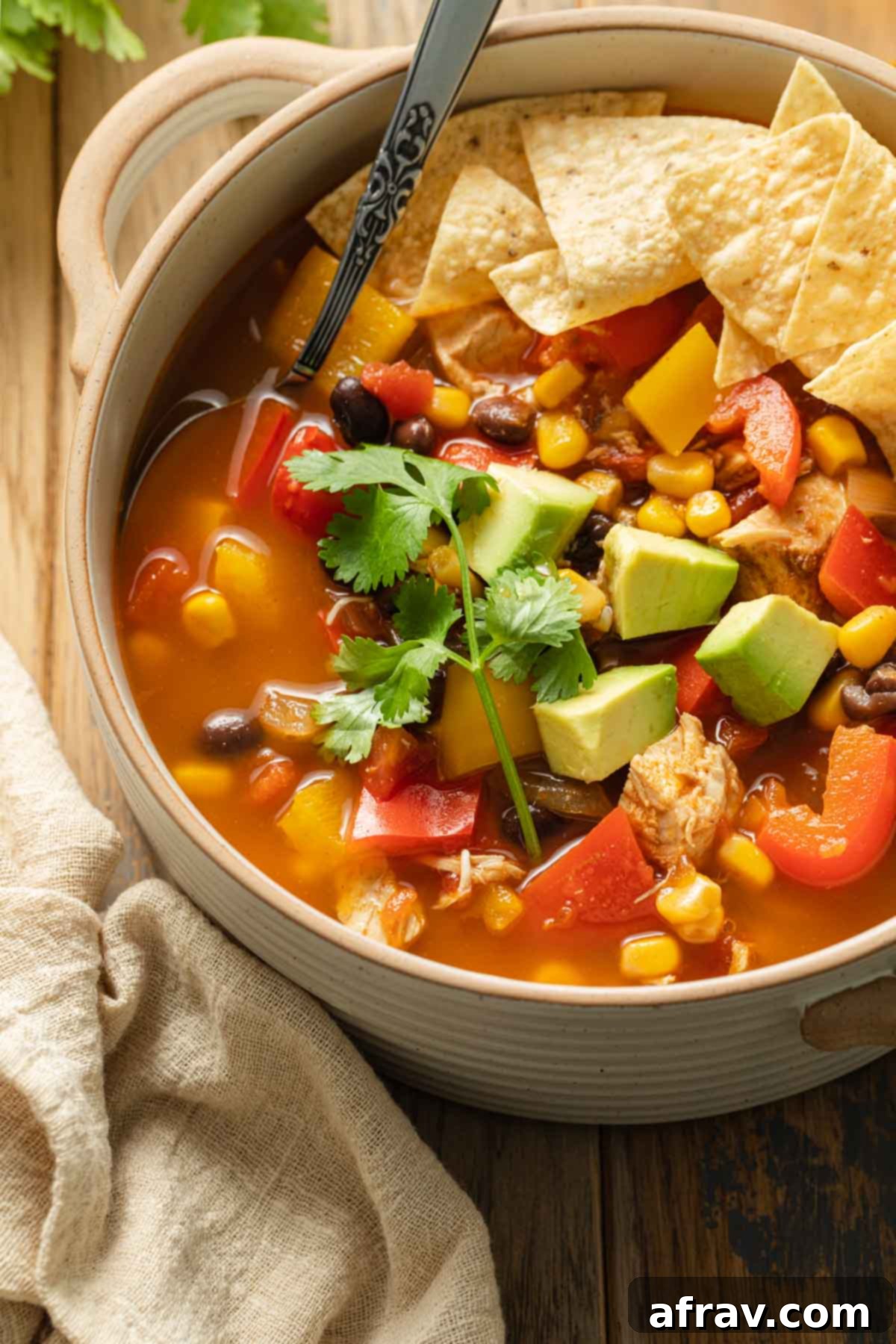 Close up view of chicken fajita soup in a beige bowl with a spoon inserted into it.