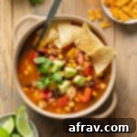 Chicken fajita soup in a beige bowl with a spoon inserted into it and tortilla chips on top.