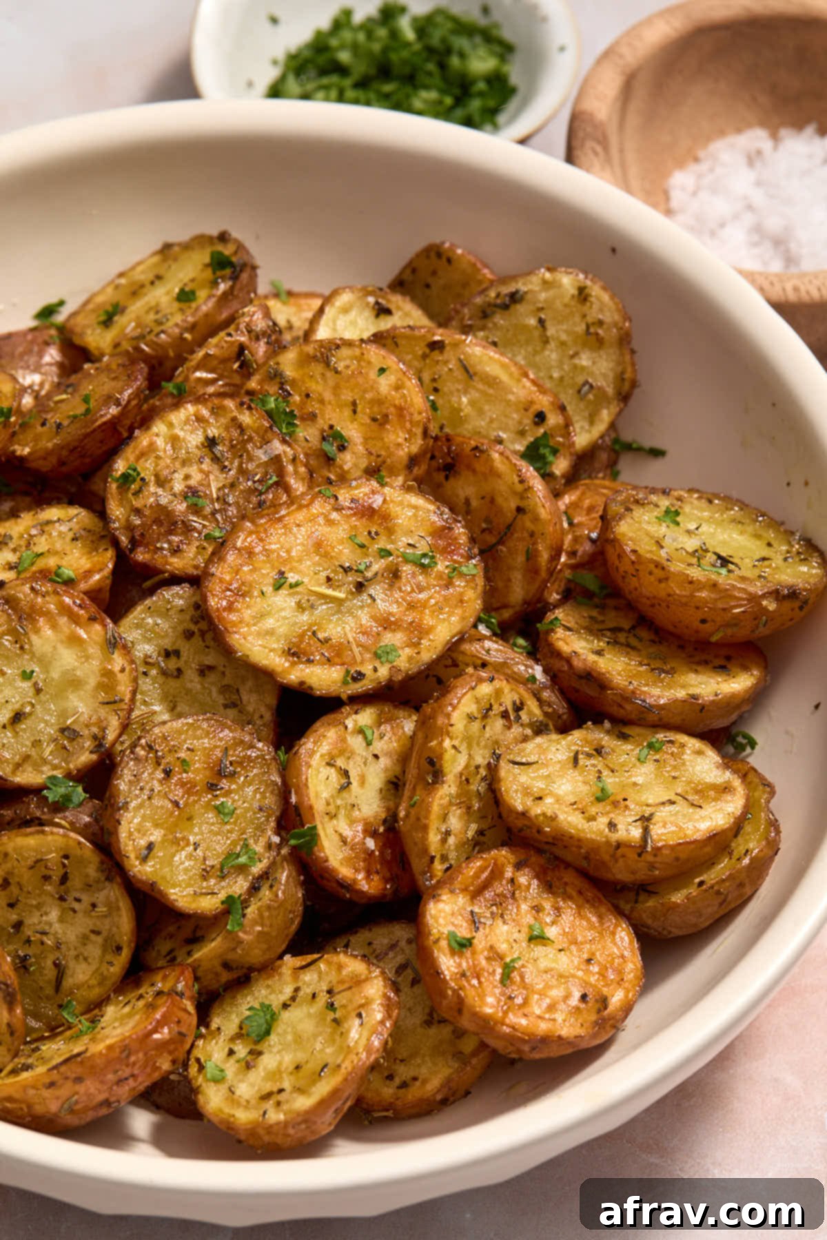 Close up of air fried baby potatoes with parsley and salt in the background.